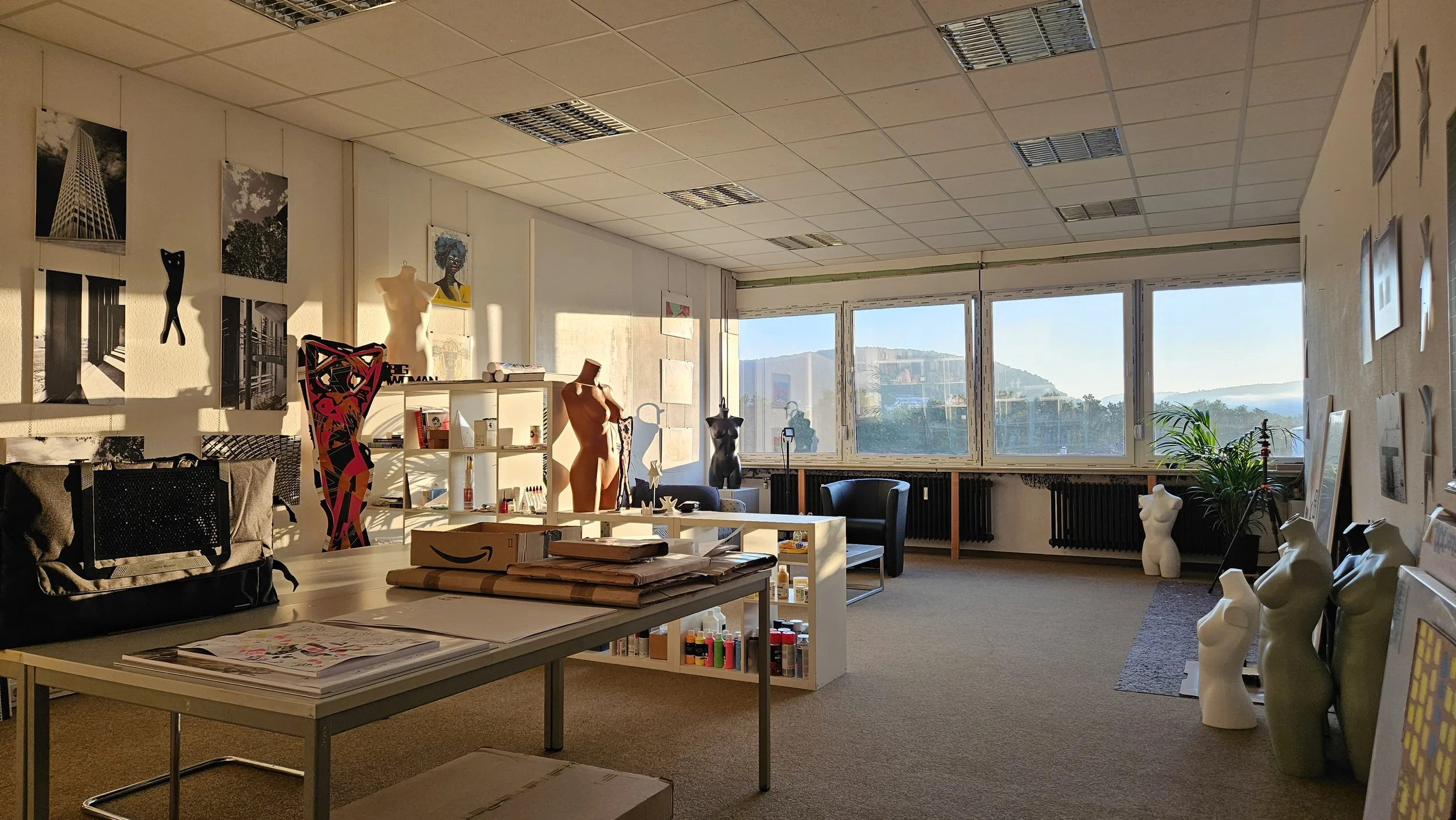 Kunststudio mit Skulpturen, Mannequins und Kunstwerken, sonnendurchfluteter Raum mit großen Fenstern und Blick auf Berge.