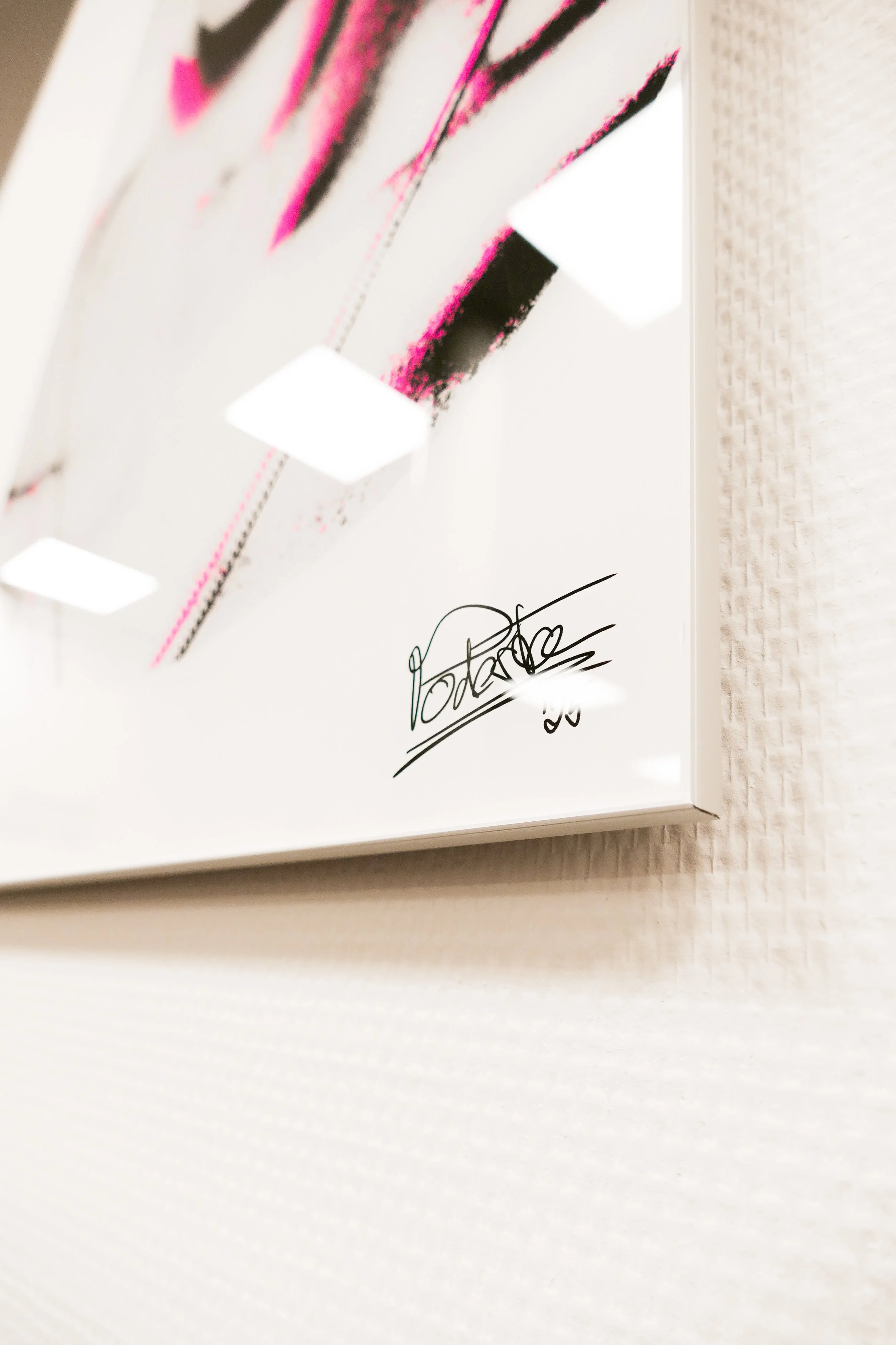 Fotobeschreibung: Ein Bild eines Drucks auf einer weißen Wand, mit pinkfarbenen und schwarzen Linien. Im unteren rechten Bereich befindet sich eine Unterschrift.