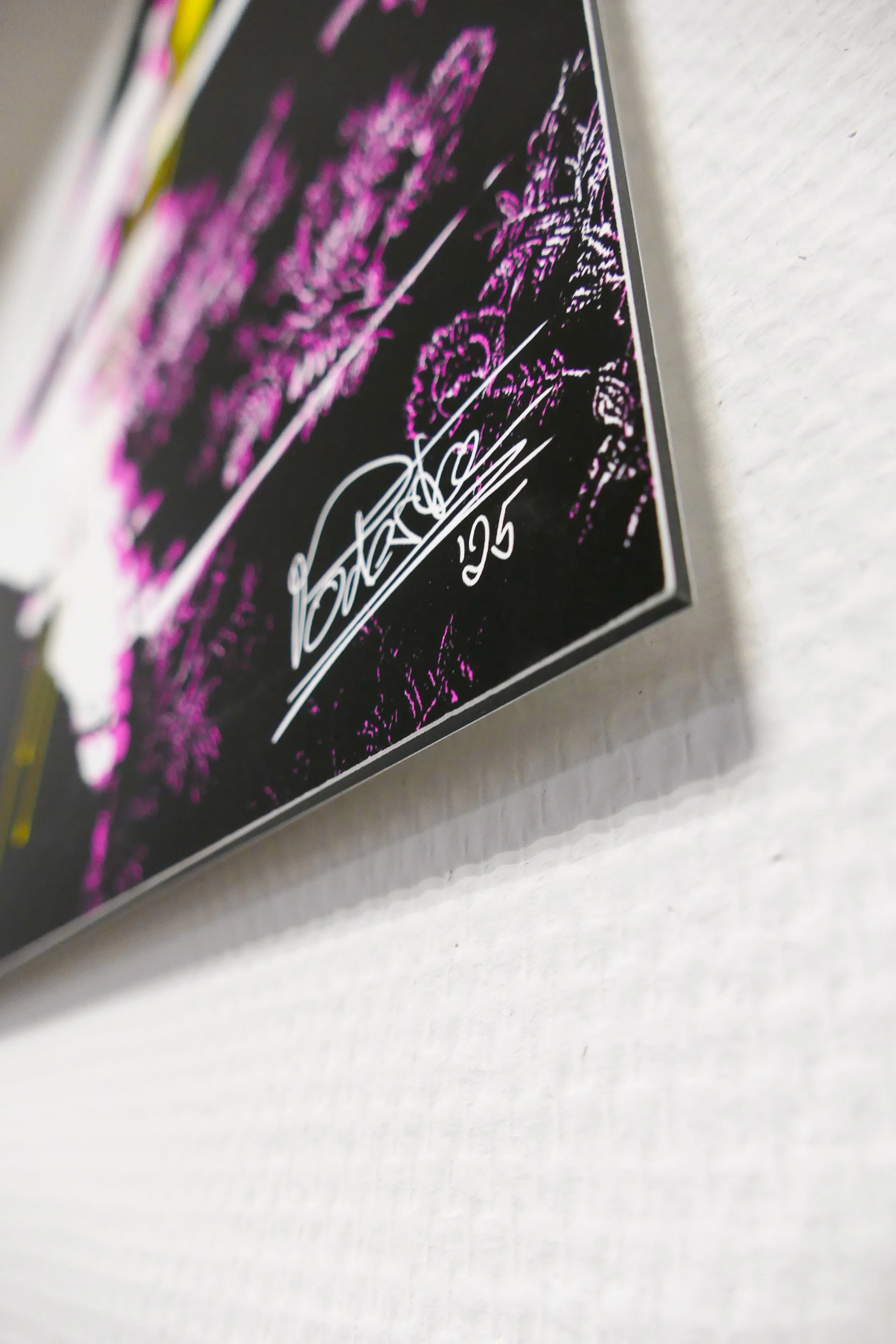 Schwarzes und pinkfarbenes Plakat mit Unterschrift und Datum 25, vermutlich ein Kunstwerk oder Poster an einer weißen Wand.