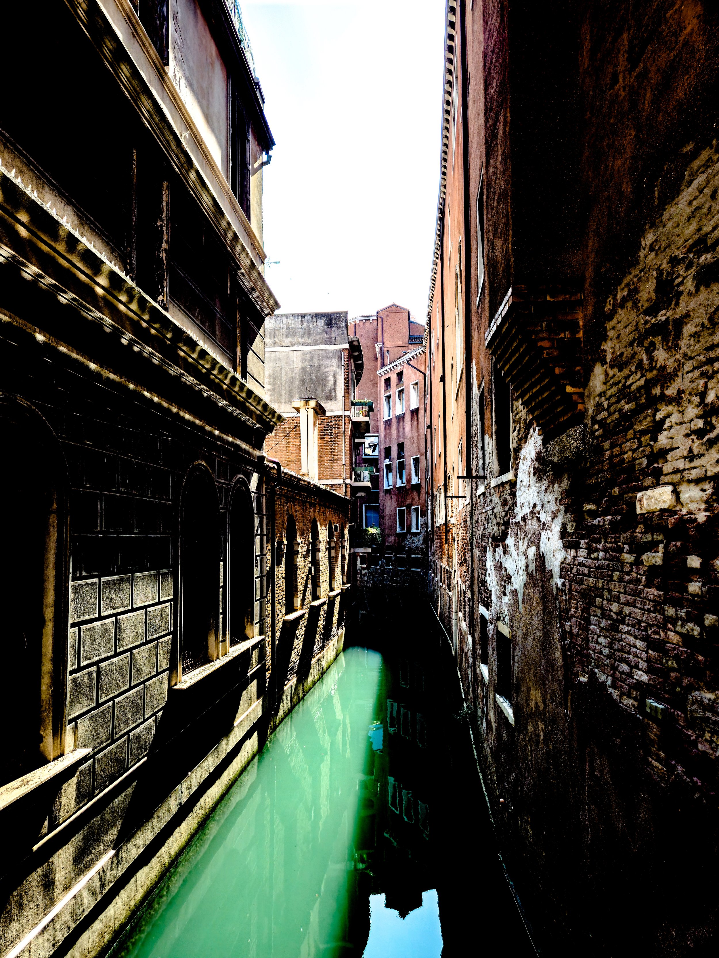 Blick durch eine enge Kanäle zwischen alten Gebäuden in Venedig, die Wasser im Kanal zeigt.