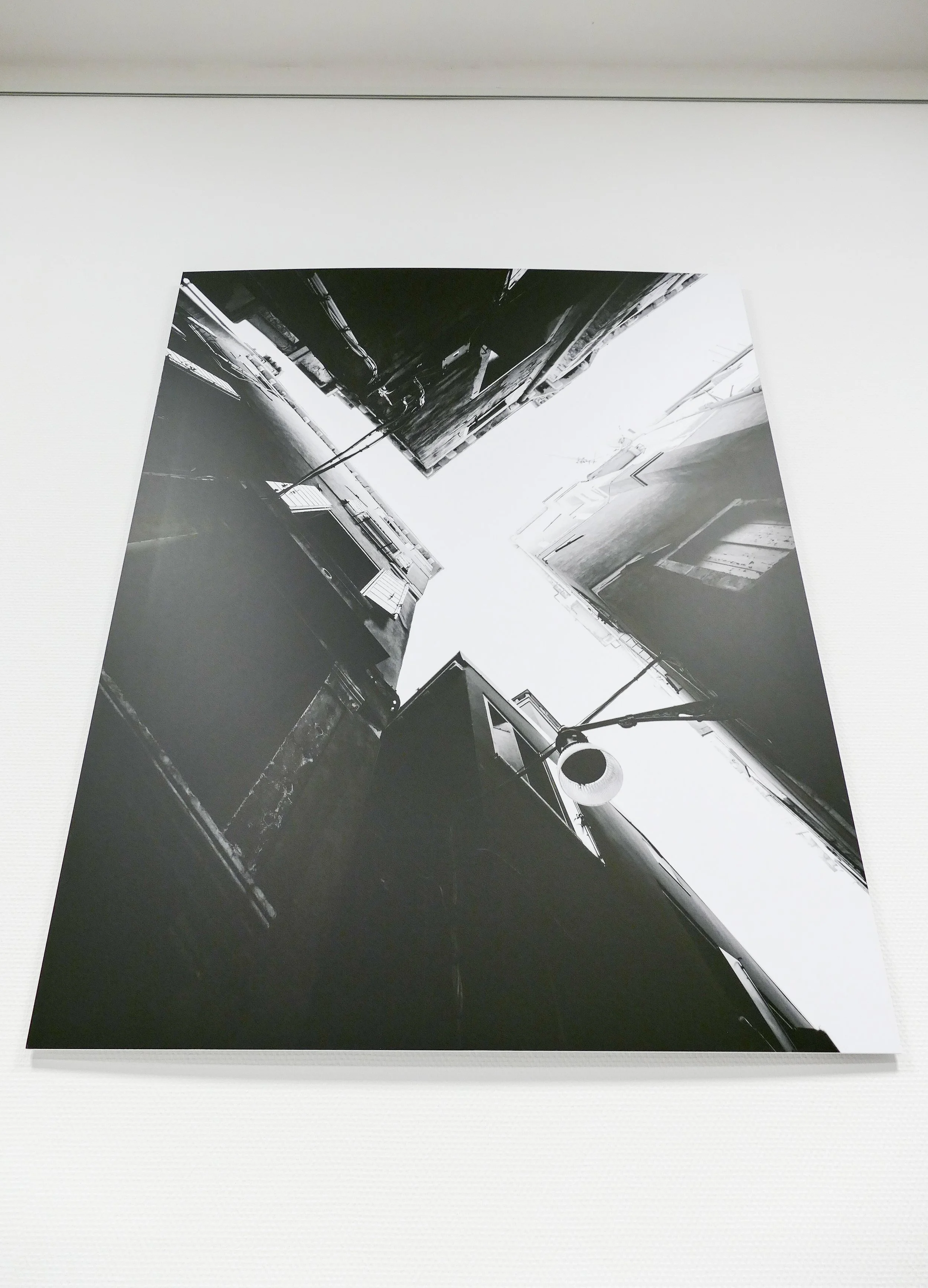 Schwarz-weiß-Fotografie von einer engen Gasse zwischen hohen Gebäuden, gesehen von unten nach oben, mit Blick auf den Himmel.