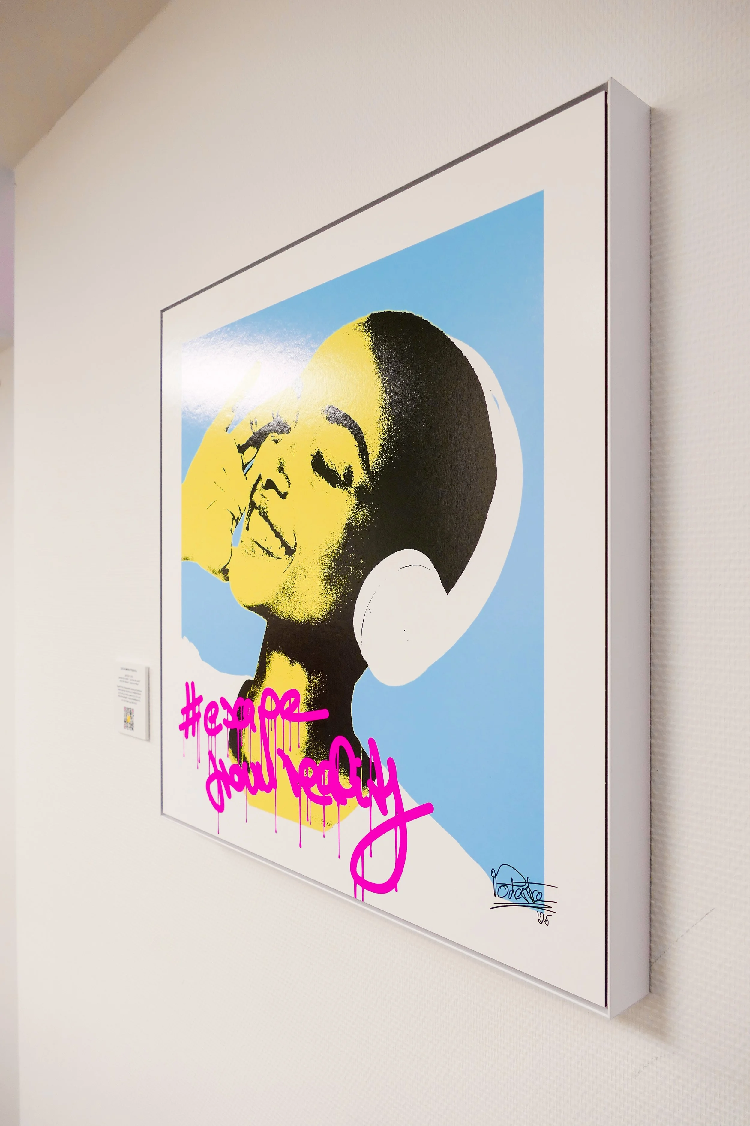 Streetart-Gemälde einer Frau mit großen weißen Kopfhörern, gelbem und schwarzem Gesicht, blauer Hintergrund, pink graffiti Schrift '#escape from reality' und auf der Leinwand.