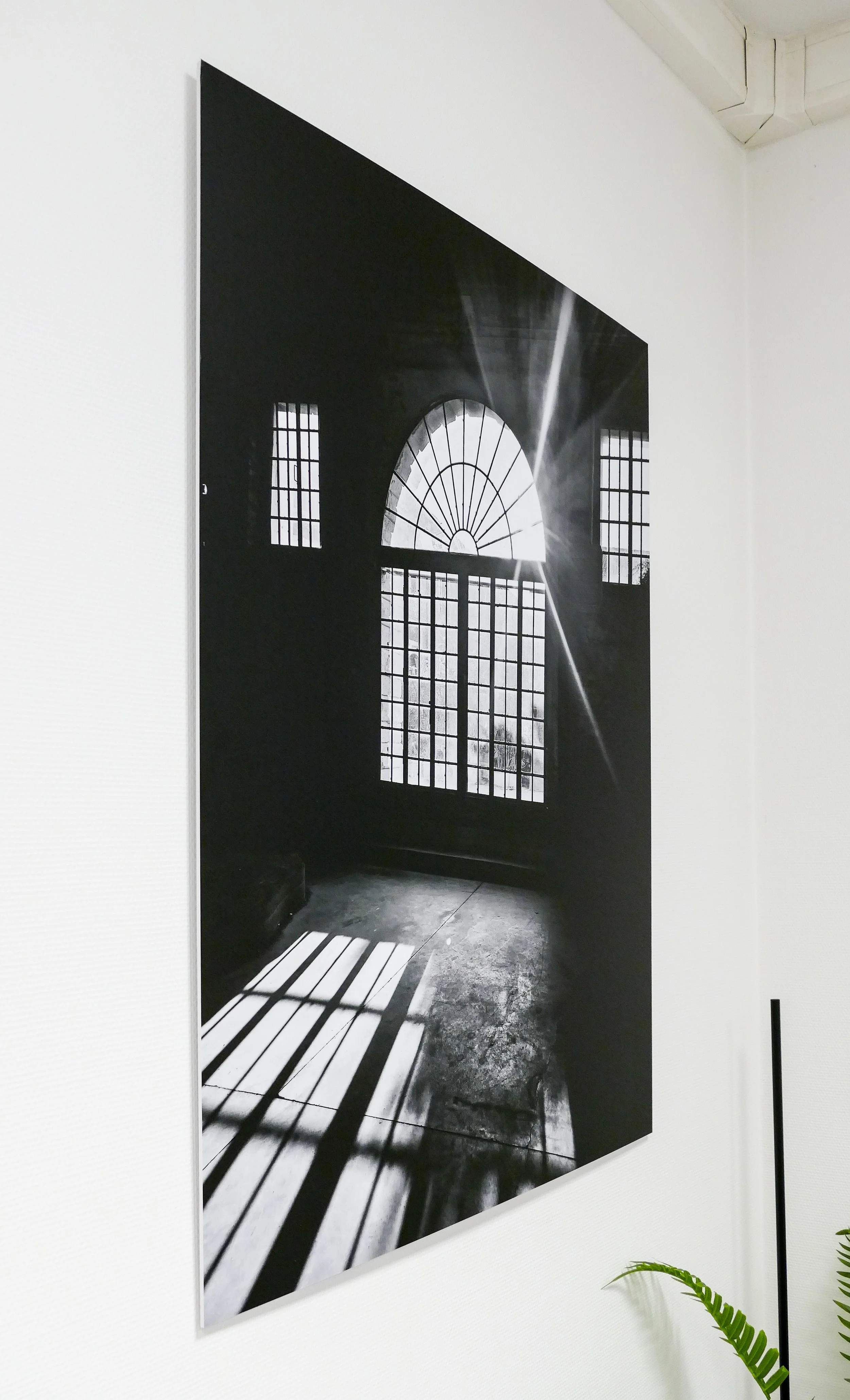 Schwarz-weiß-Fotografie eines Sonnenlichts, das durch große Fenster in einem dunklen Raum mit Gittermustern auf den Boden fällt.