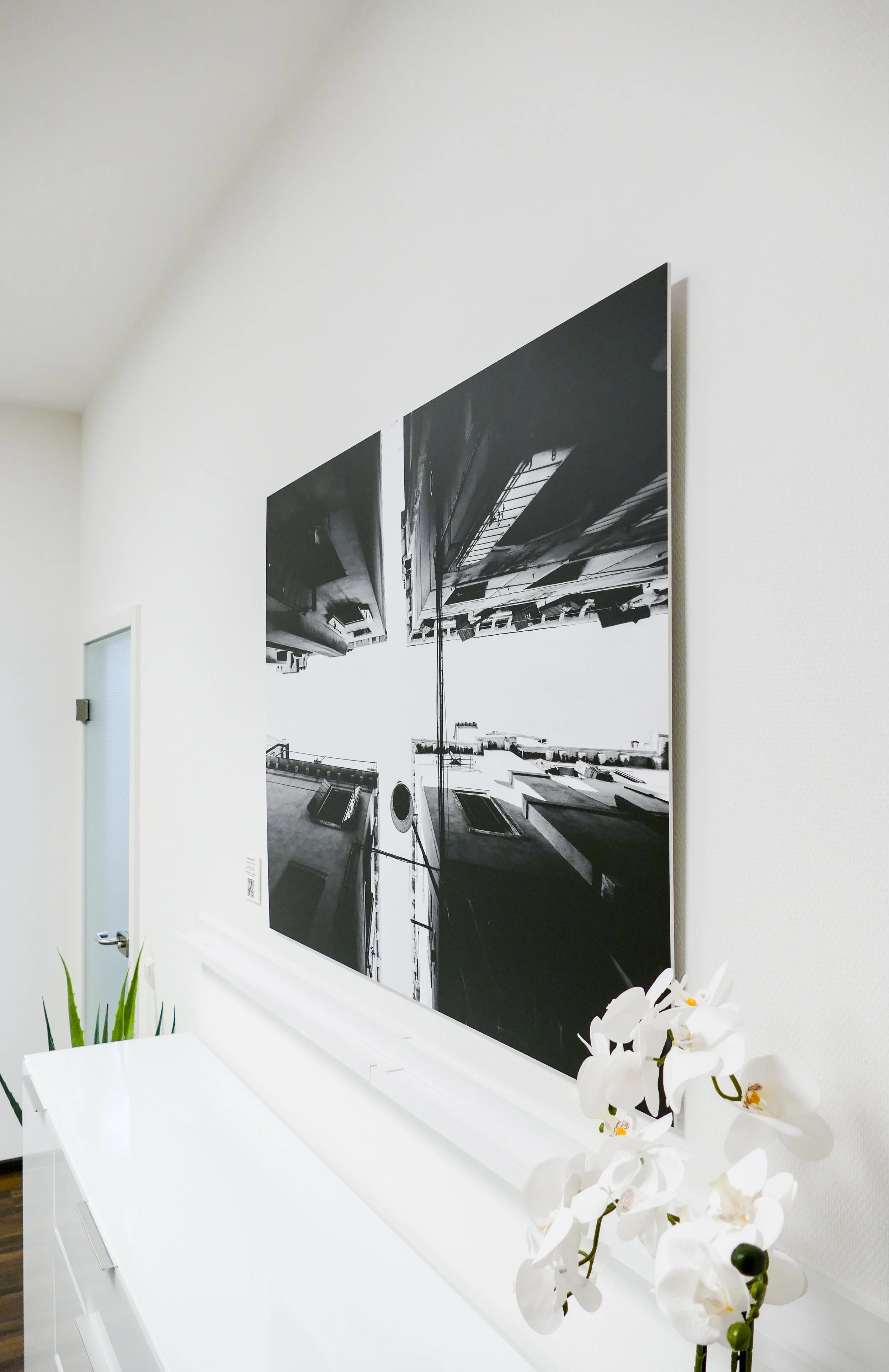 Schwarz-weiß-Fotografie eines urbanen Stadtbilds, die an einer weißen Wand hängt, mit weißen Orchideen im Vordergrund.