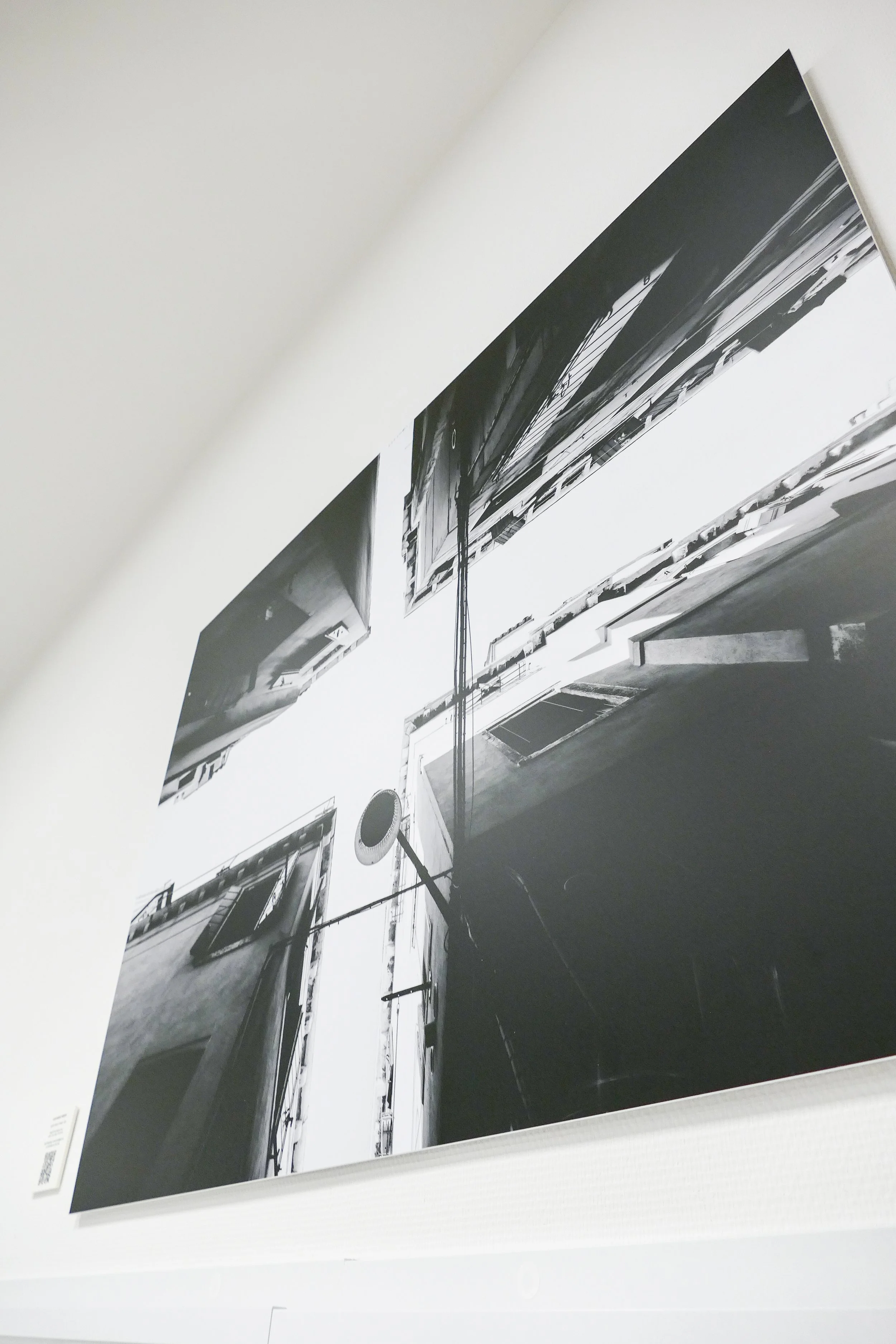 Schwarz-weiße Fotografie eines engen Innenhofs zwischen Gebäuden, aufgenommen von unten, mit mehreren Fenstern und einer Antenne.