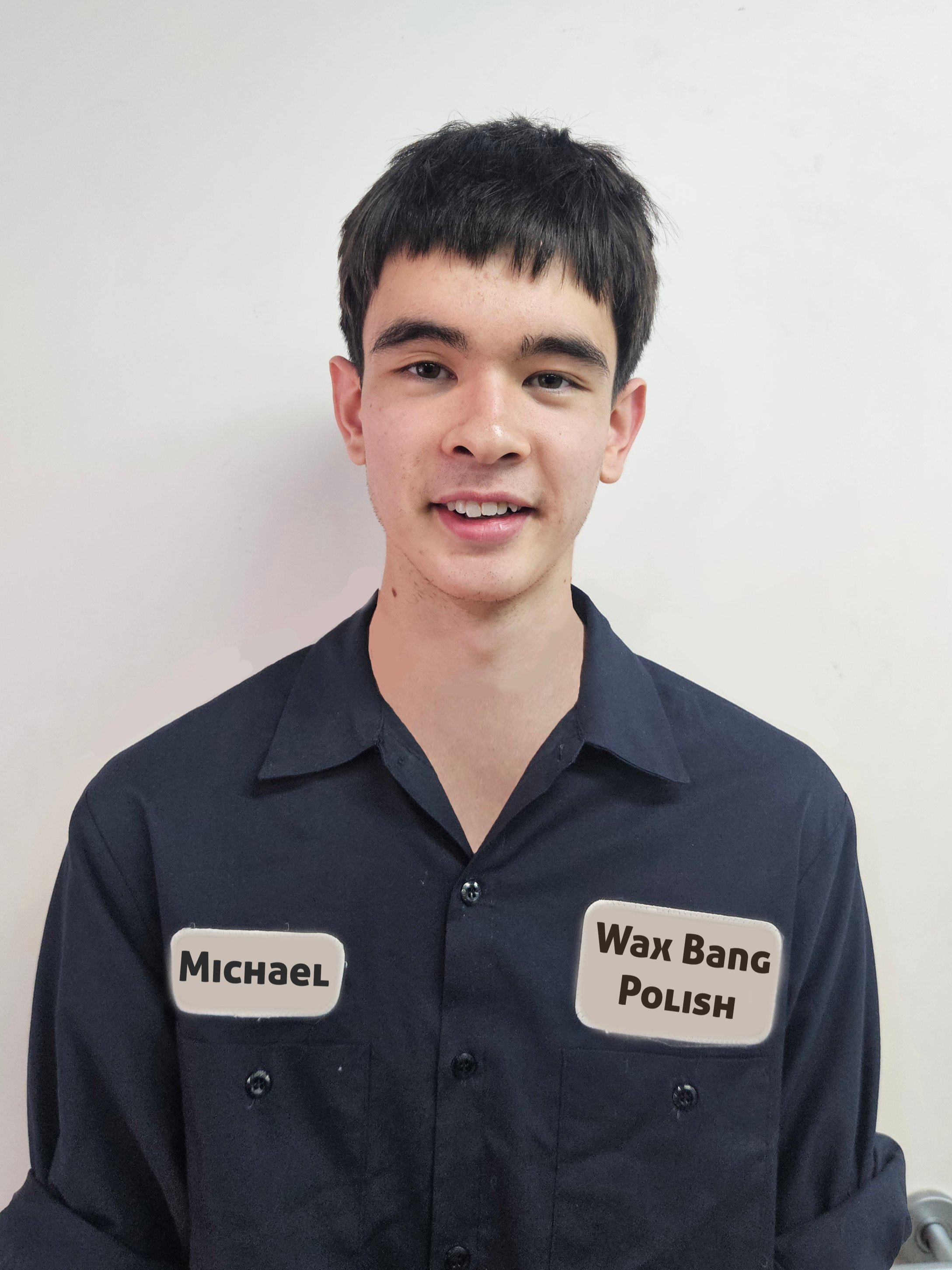 Young man with short dark hair, wearing a black shirt, smiling, standing in front of a white door. Name tags read 'Michael' and 'Wax Bang Polish'.