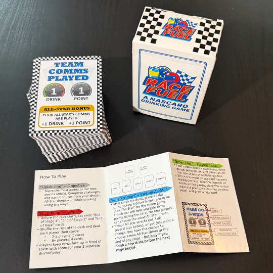 A box of Race Fuel Nascar drinking game, a deck of cards with Team Comms Played shown, and an instruction booklet with game instructions and rules on a black surface.