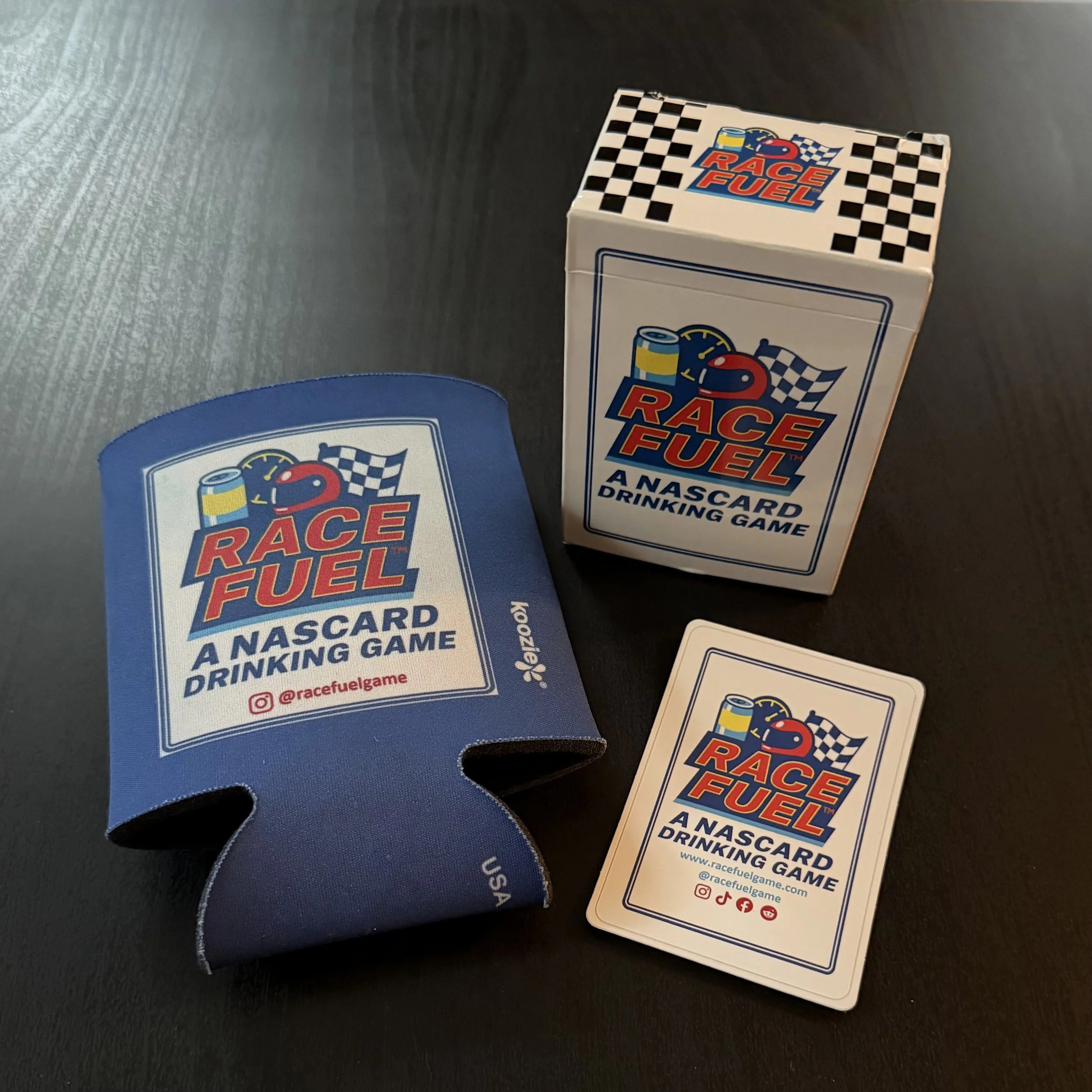 Business cards for Race Fuel, a Nascar drinking game, with social media icons and website information, placed on a dark surface.