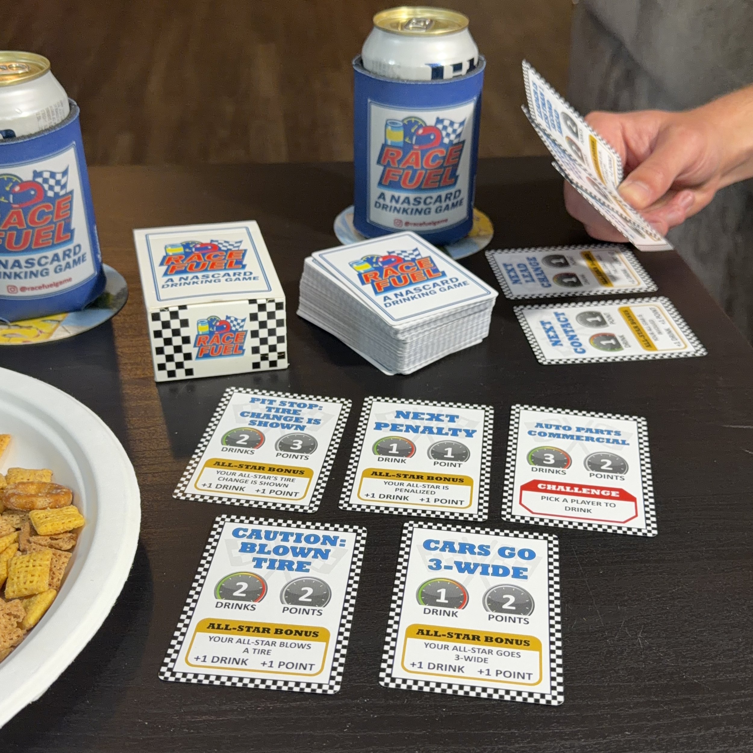 Race Fuel card game setup with cards, box, can sleeves, and a player dealing cards during race day.