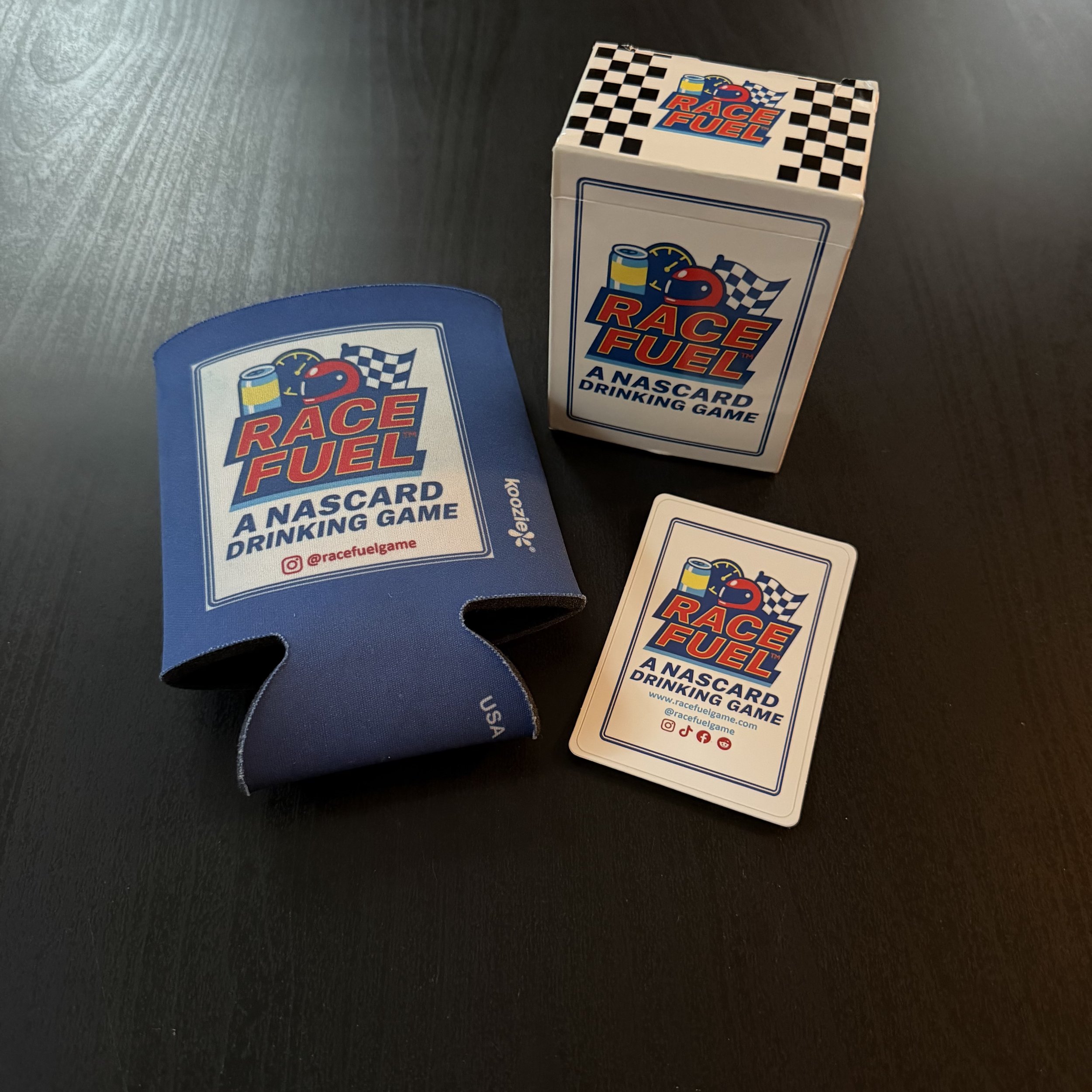 Cards and a box for the game Race Fuel, a Nascar drinking game, on a black surface.