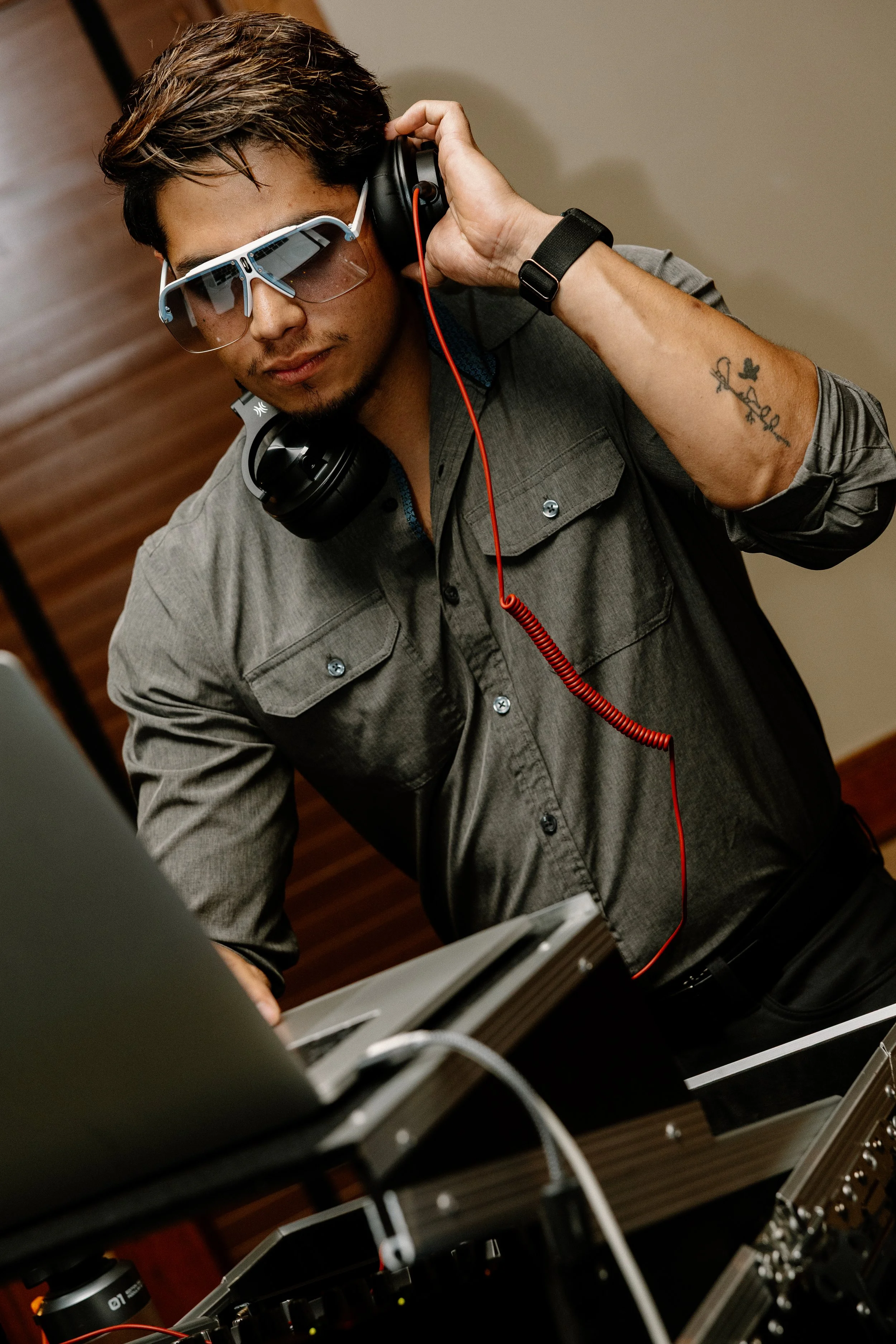 A man wearing sunglasses and headphones, focusing on a synthesizer keyboard, possibly performing music or DJing.