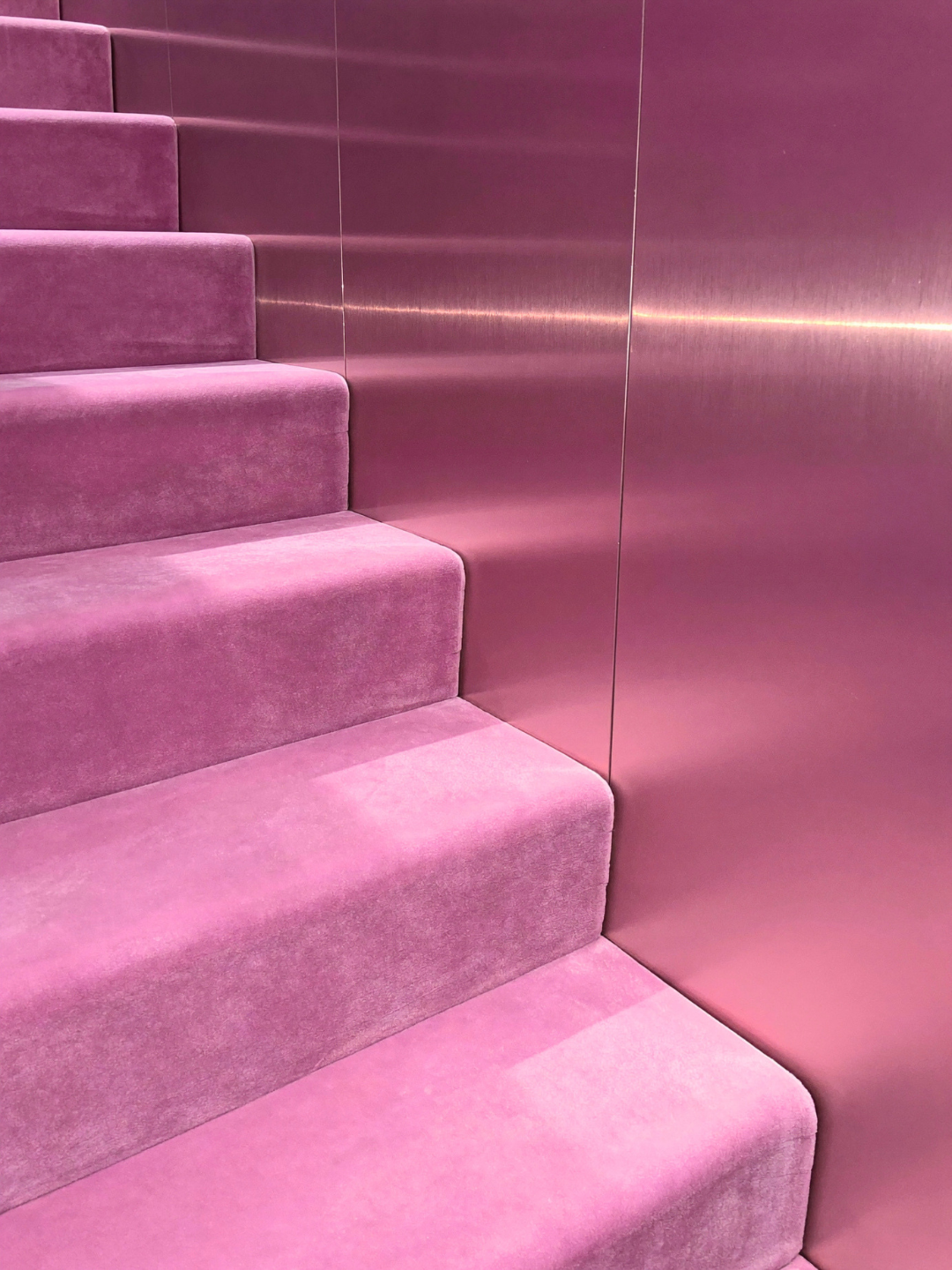 Pink velvet staircase adjacent to shiny pink metallic wall.