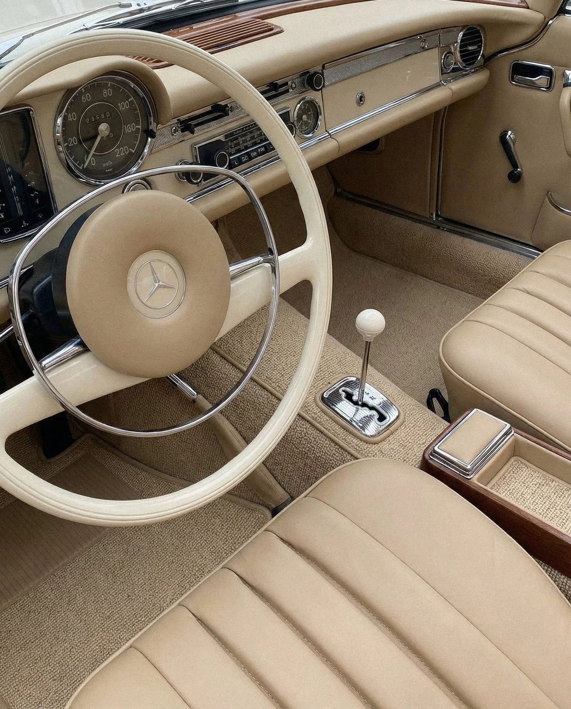 Interior of a vintage beige Mercedes-Benz car, showcasing the dashboard, steering wheel, gear shift, and front bench seat.