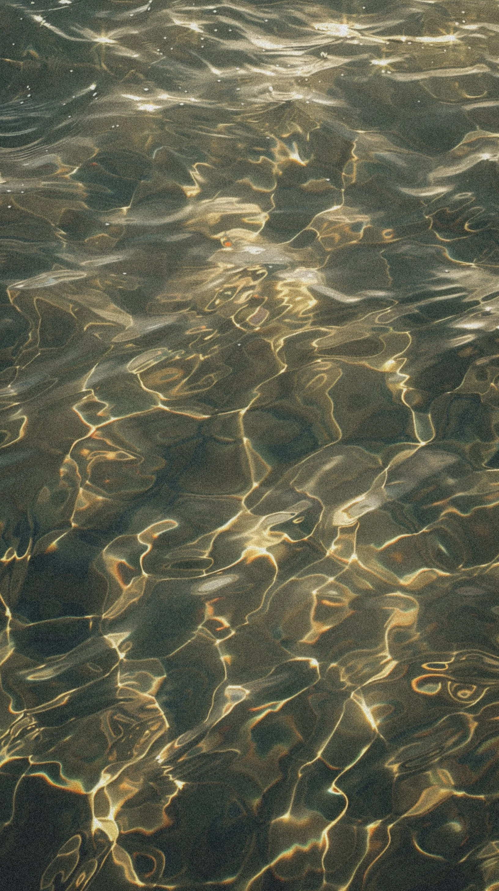 Close-up of sunlight reflecting on the surface of water, creating intricate patterns with light and dark areas.