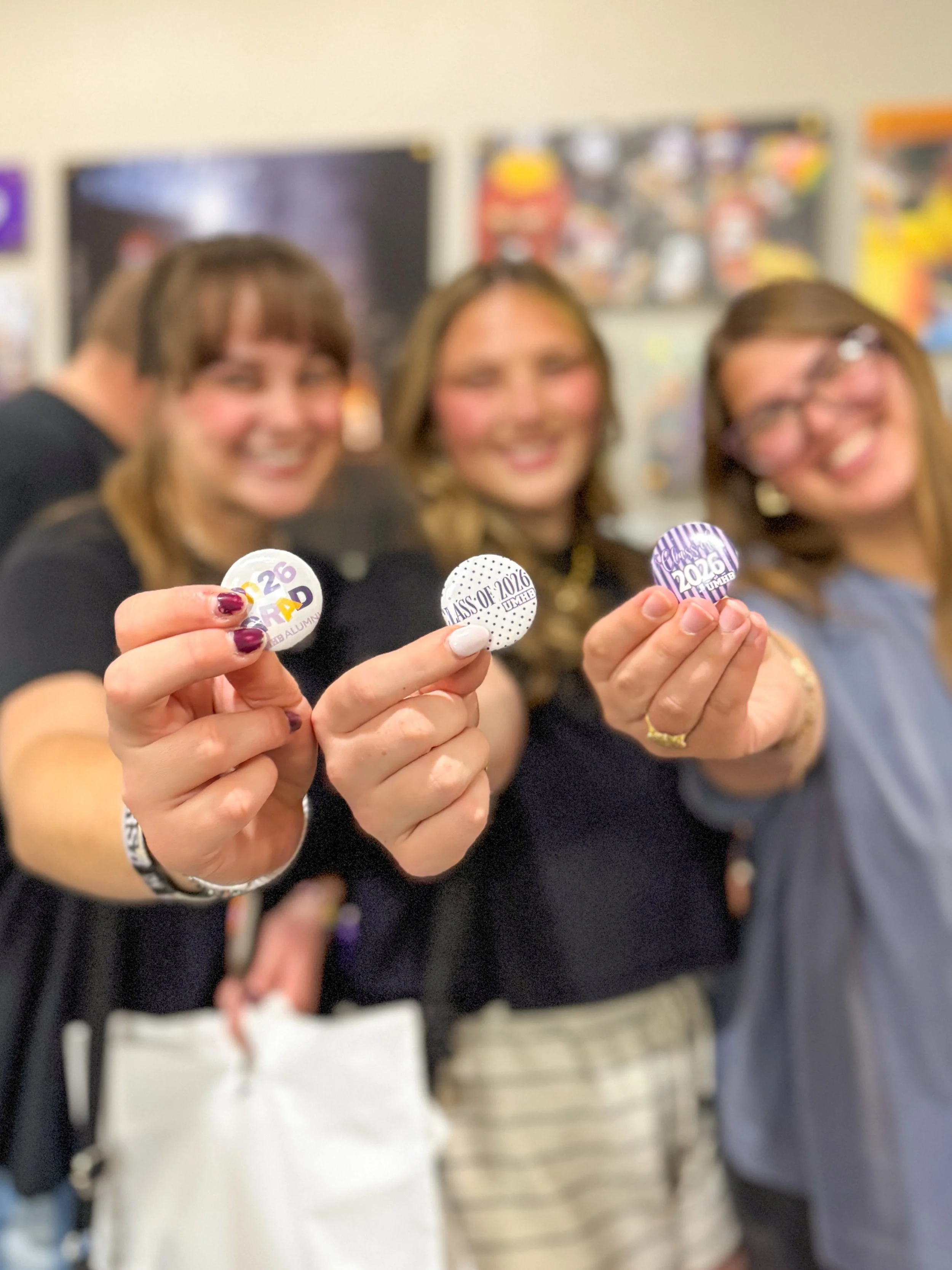 Three people holding up pins or badges with graduation year and name, celebrating graduation.