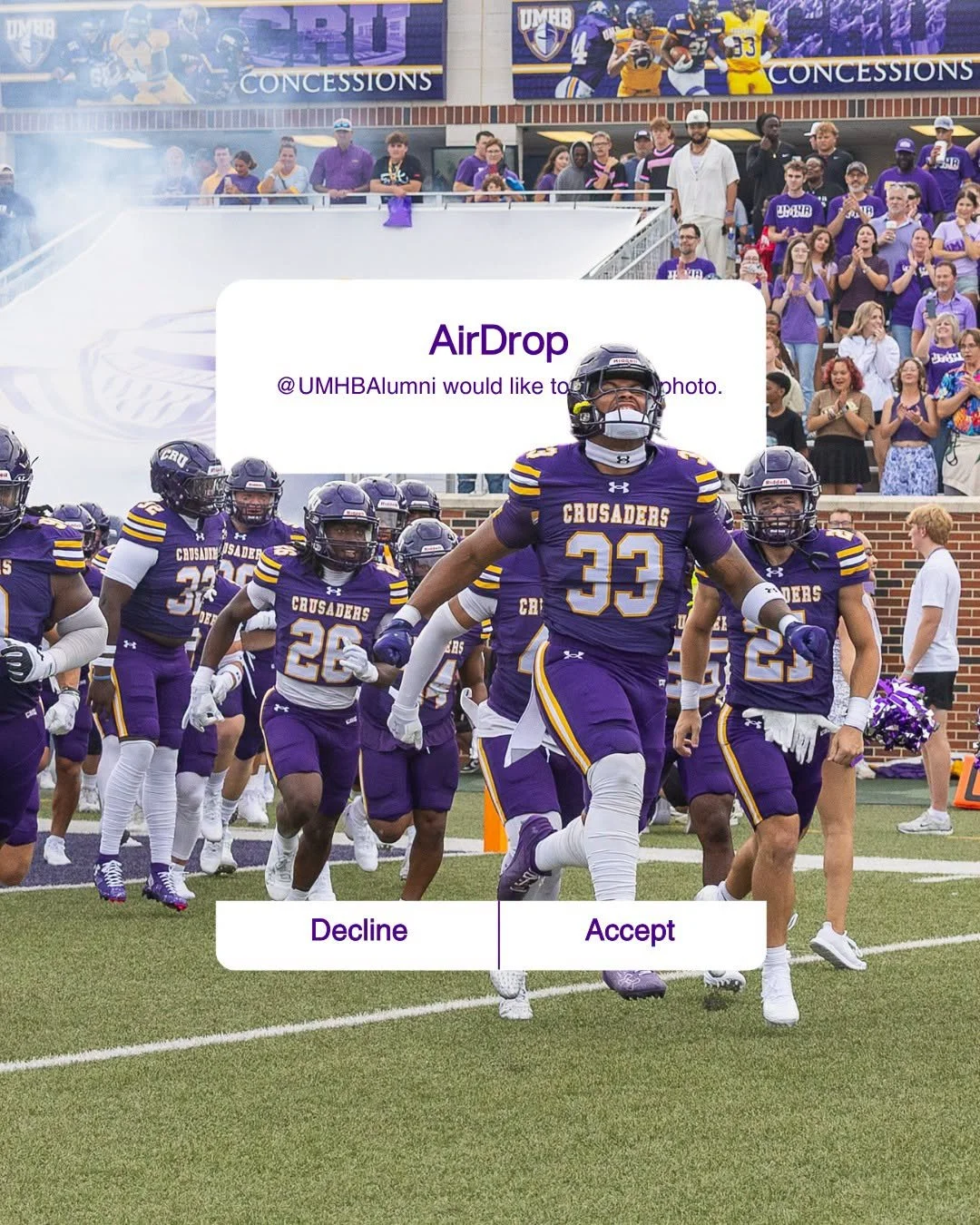 Football players from the Crusaders team in purple uniforms running onto the field with crowd in the background, during a game or event.
