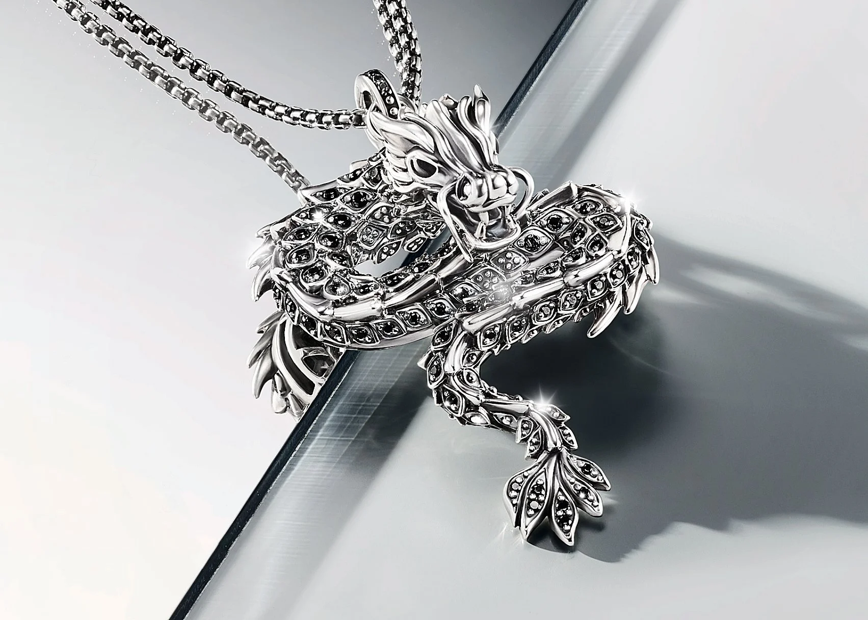 A Thomas Sabo silver dragon pendant necklace with black gemstones, resting on a reflective surface.