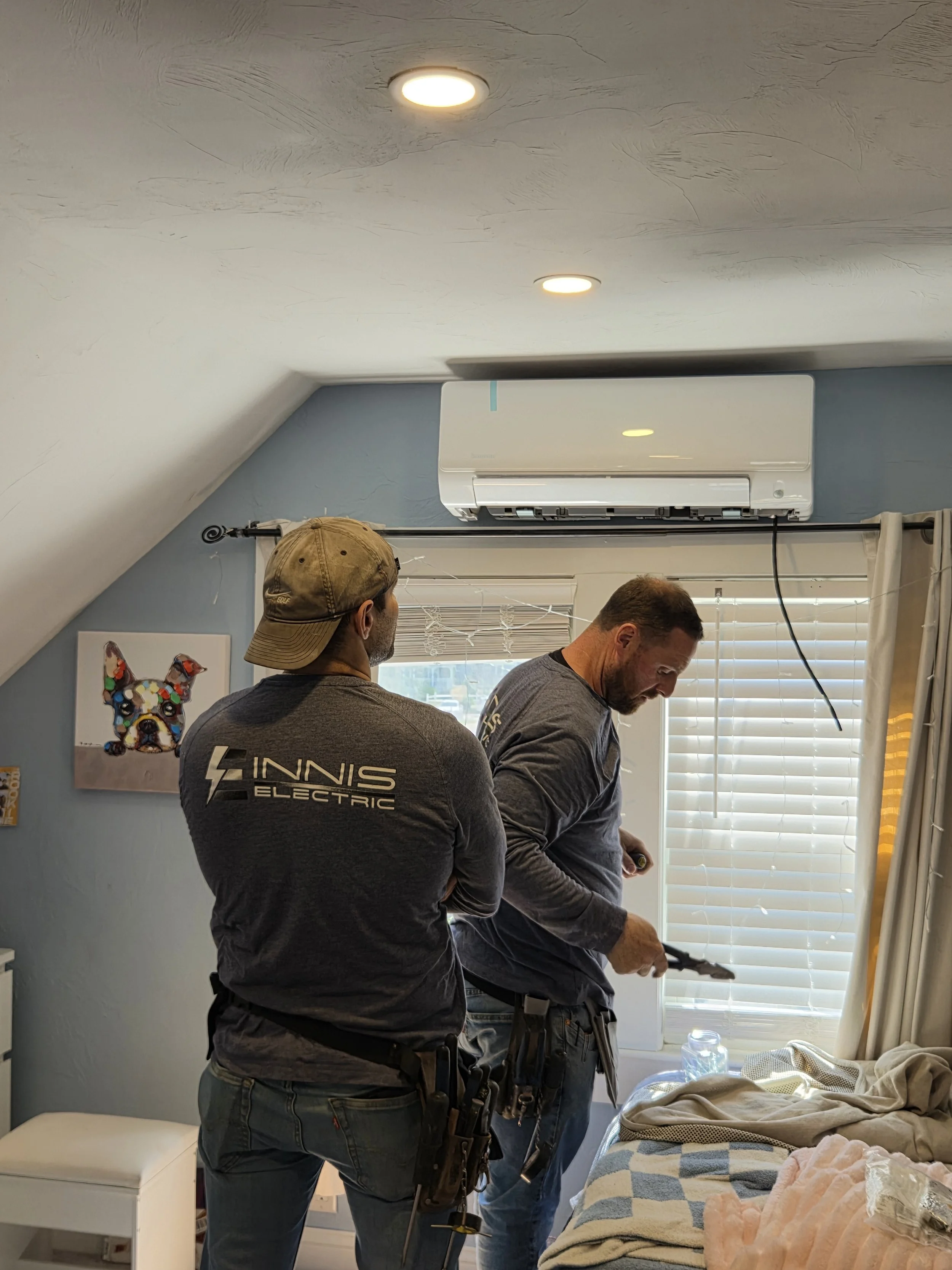 An outdoor heat pump or air conditioning unit mounted on a wall of a house with a stone exterior.