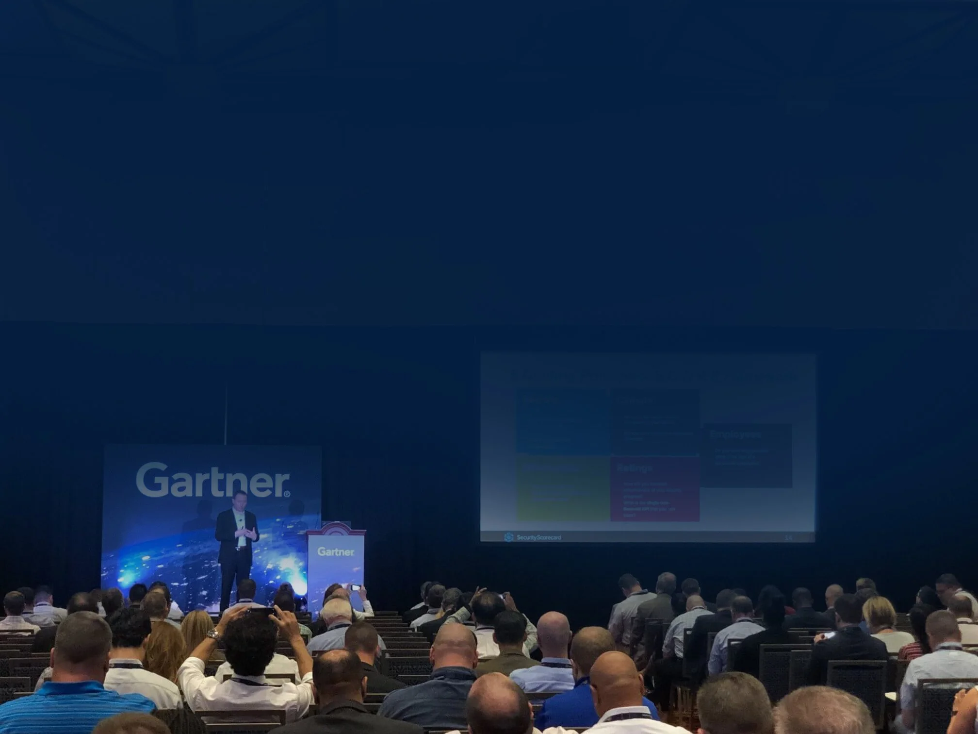 Dr. Aleksandr Yampolskiy | Cybersecurity Expert presenting on stage at a conference with a large screen displaying a presentation, audience seated in front, and "Gartner" branding on stage backdrop.