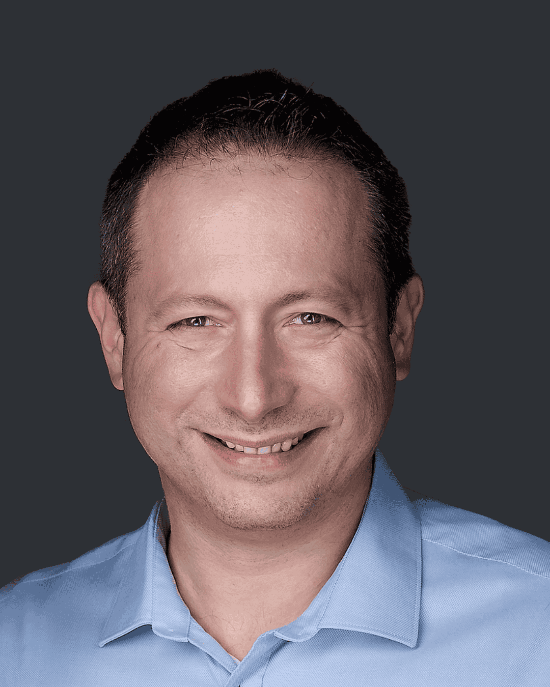 Headshot of Dr. Aleksandr Yampolskiy | Cybersecurity Expert & CEO of SecurityScorecard smiling man with short dark hair, wearing a light blue collared shirt, against a dark background.