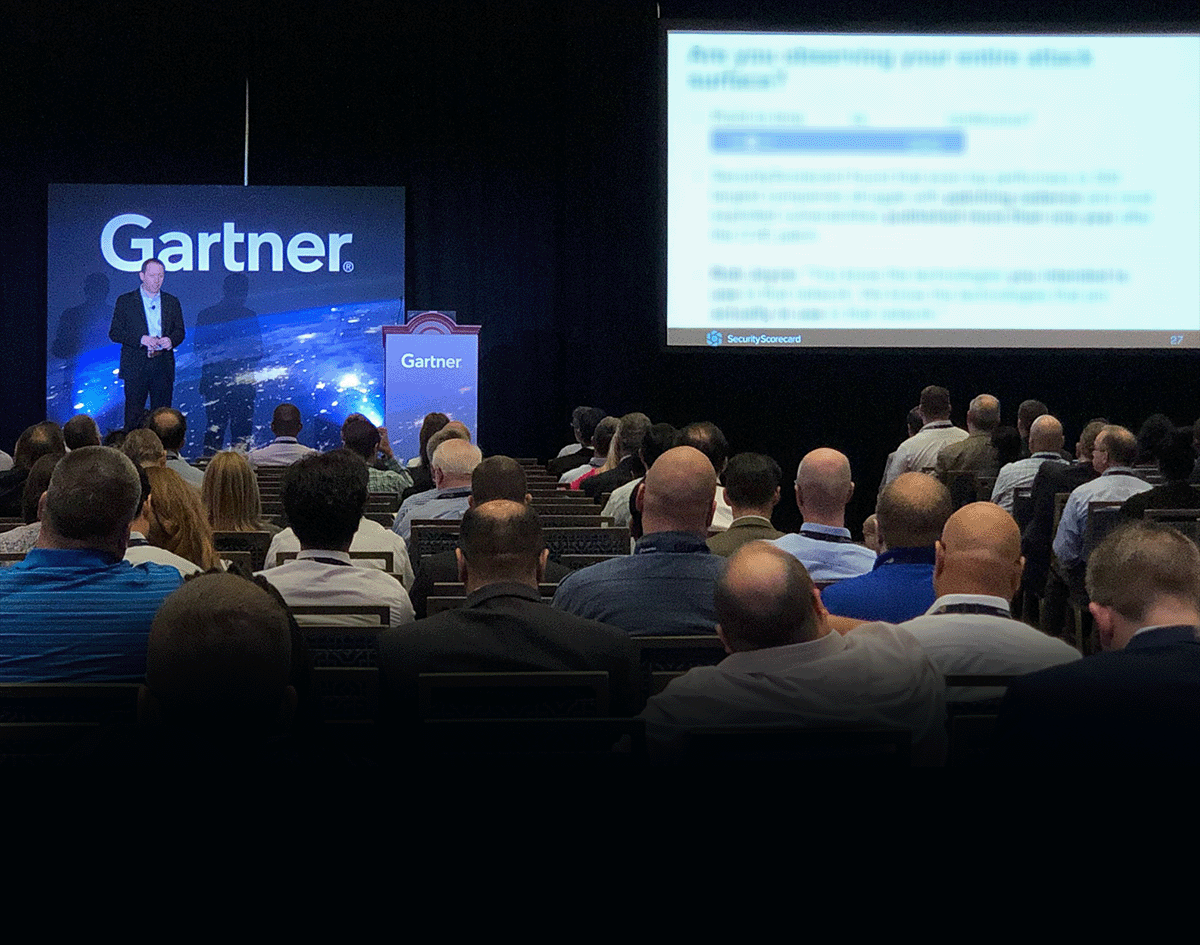 Dr. Aleksandr Yampolskiy | Cybersecurity Expert & CEO of SecurityScorecard on stage at a conference with a large screen behind him displaying a presentation, the audience seated and watching.