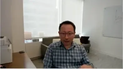 Dr. Aleksandr Yampolskiy | Cybersecurity Expert & CEO of SecurityScorecard in glasses and checkered shirt sitting at desk in an office with whiteboard and window.
