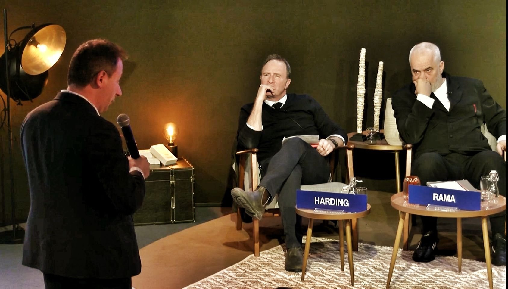 Two men sitting on chairs with nameplates labeled 'HARDING' and 'RAMA' participate in a discussion, while Dr. Aleksandr Yampolskiy | Cybersecurity Expert & CEO of SecurityScorecard stands in front holding a microphone.