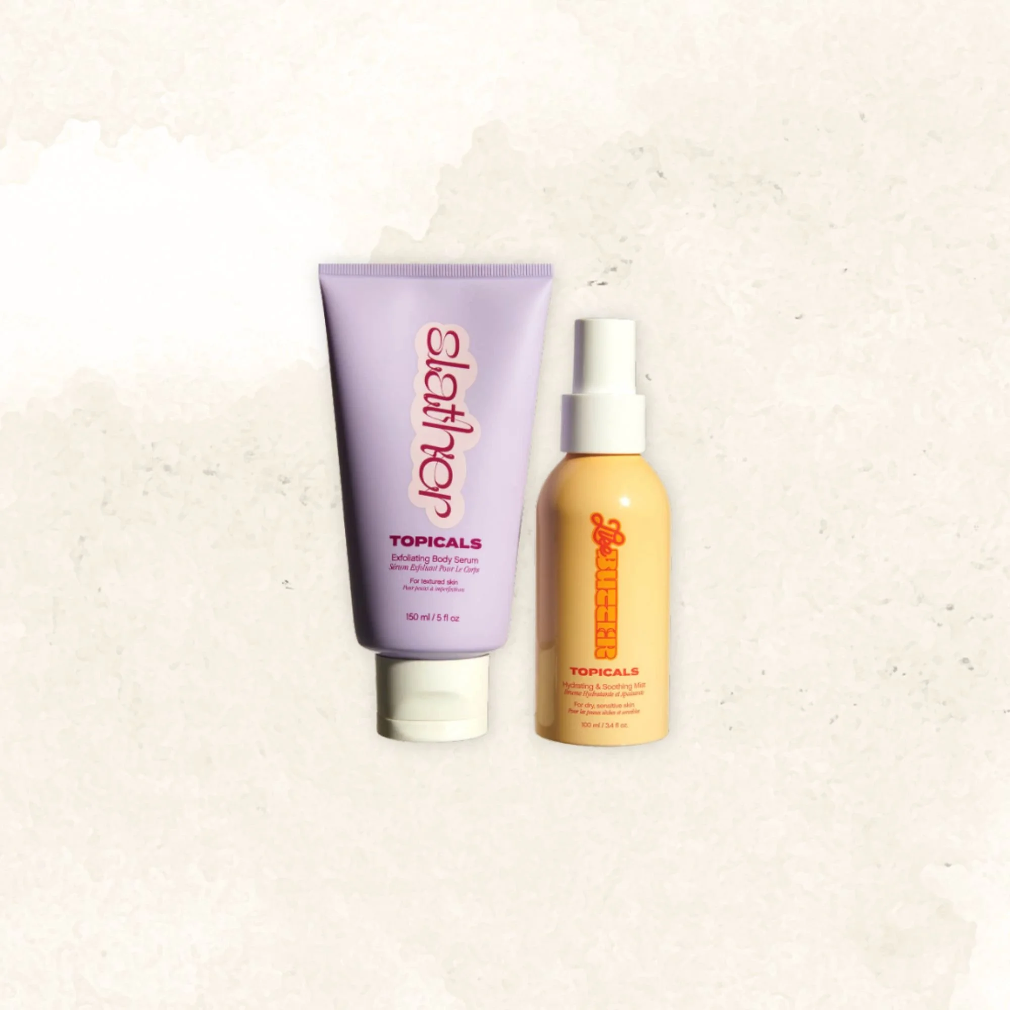 Two skincare products from the brand 'SABRE' and 'TOPICALS' on a white textured background. One is a lavender-colored tube labeled 'Exfoliating Body Serum' and the other is an orange spray bottle labeled 'Hydrating & Soothing Mist.'