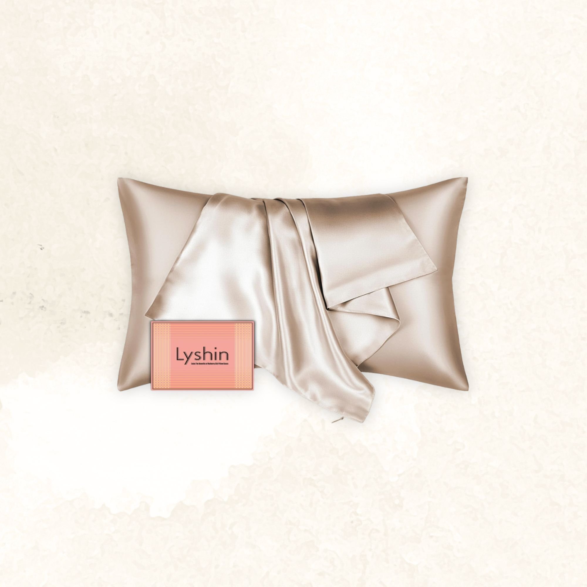 A silver satin pillow with a matching satin gown draped on top, and a small pink card with the word 'Lyshin' placed in front.