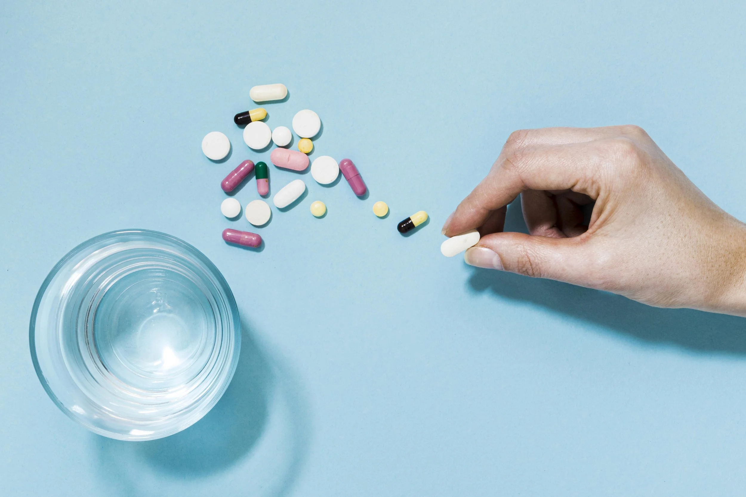 Scattered pills on a table with a person picking a single pill - Integrative Healthcare Alliance