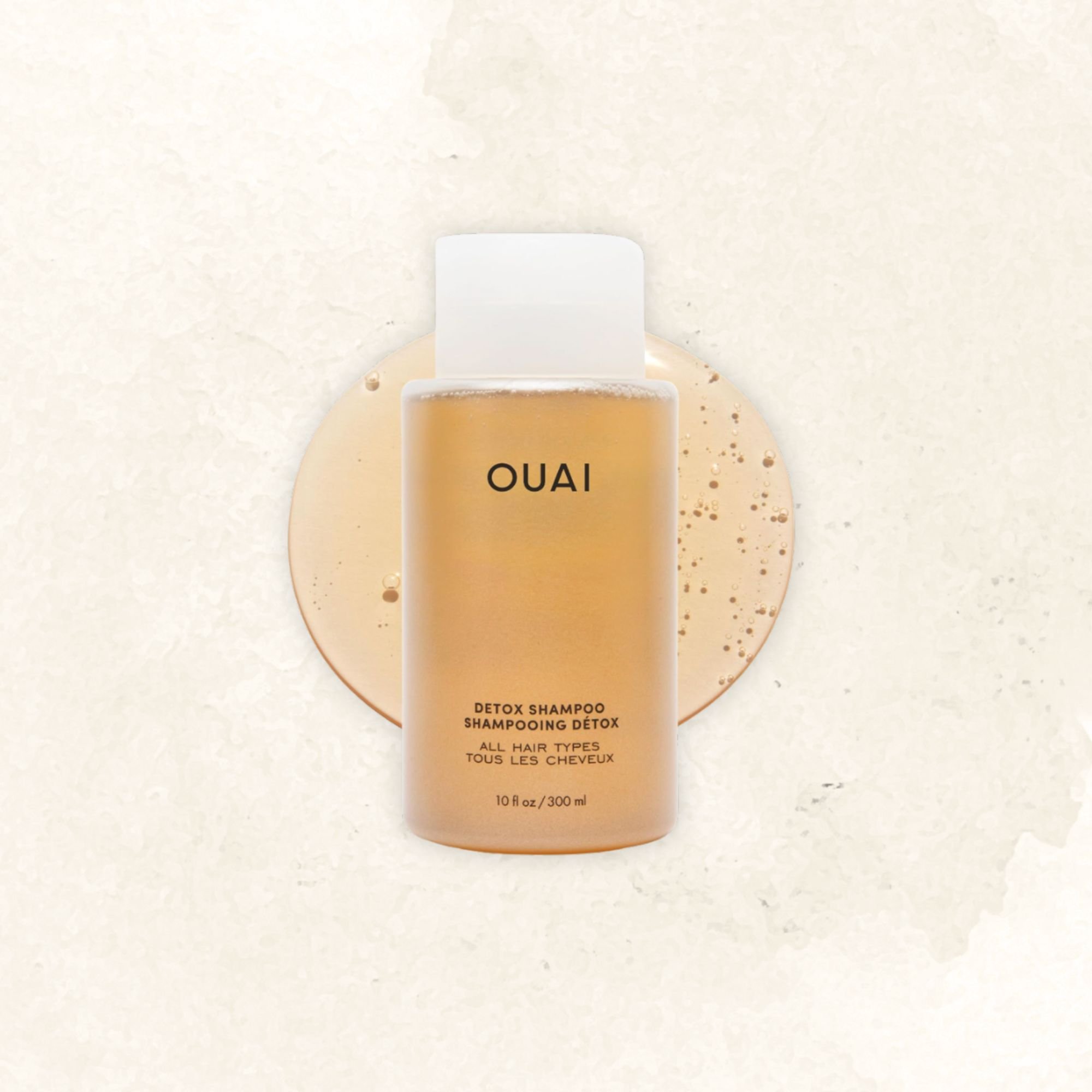 A bottle of OUAI Detox Shampoo with some spilled shampoo on a white surface.