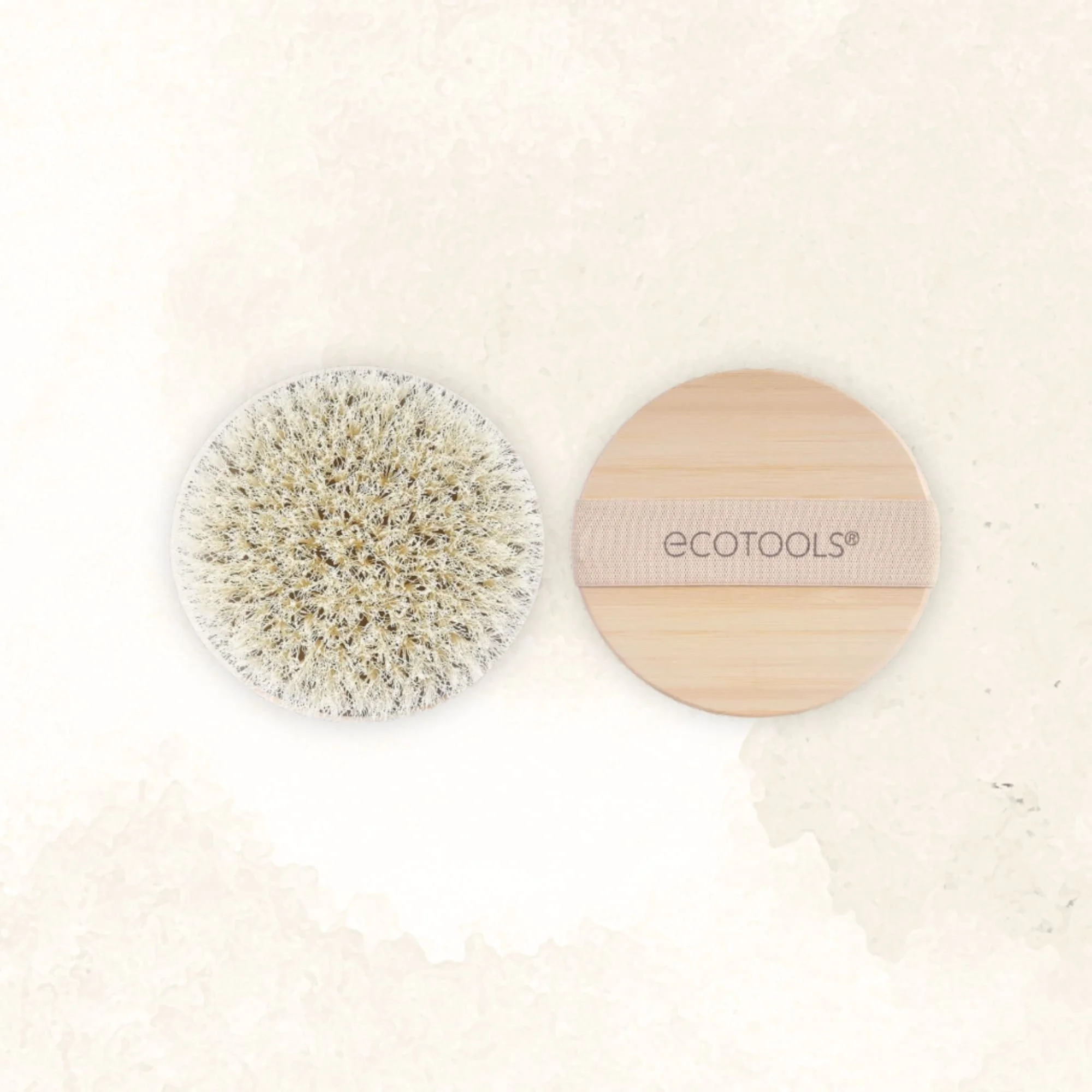 A round exfoliating brush with a beige handle and an empty round wooden container with the brand name 'EcoTools' on the cover.