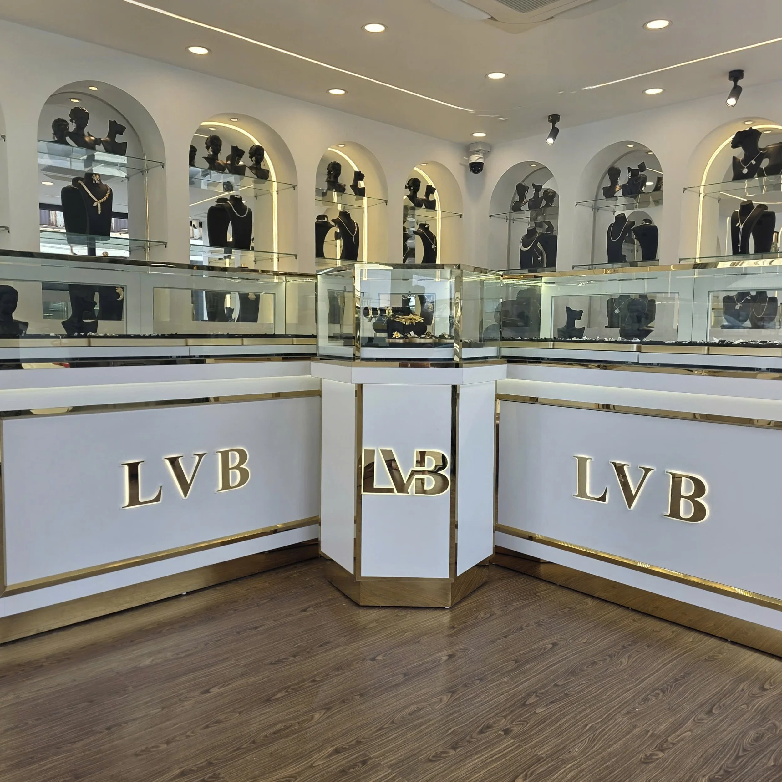Jewelry display case in a store with necklaces and bust forms showcasing jewelry, and the store features a white and gold color scheme with the letters 'LVB' on the front of the display counter.