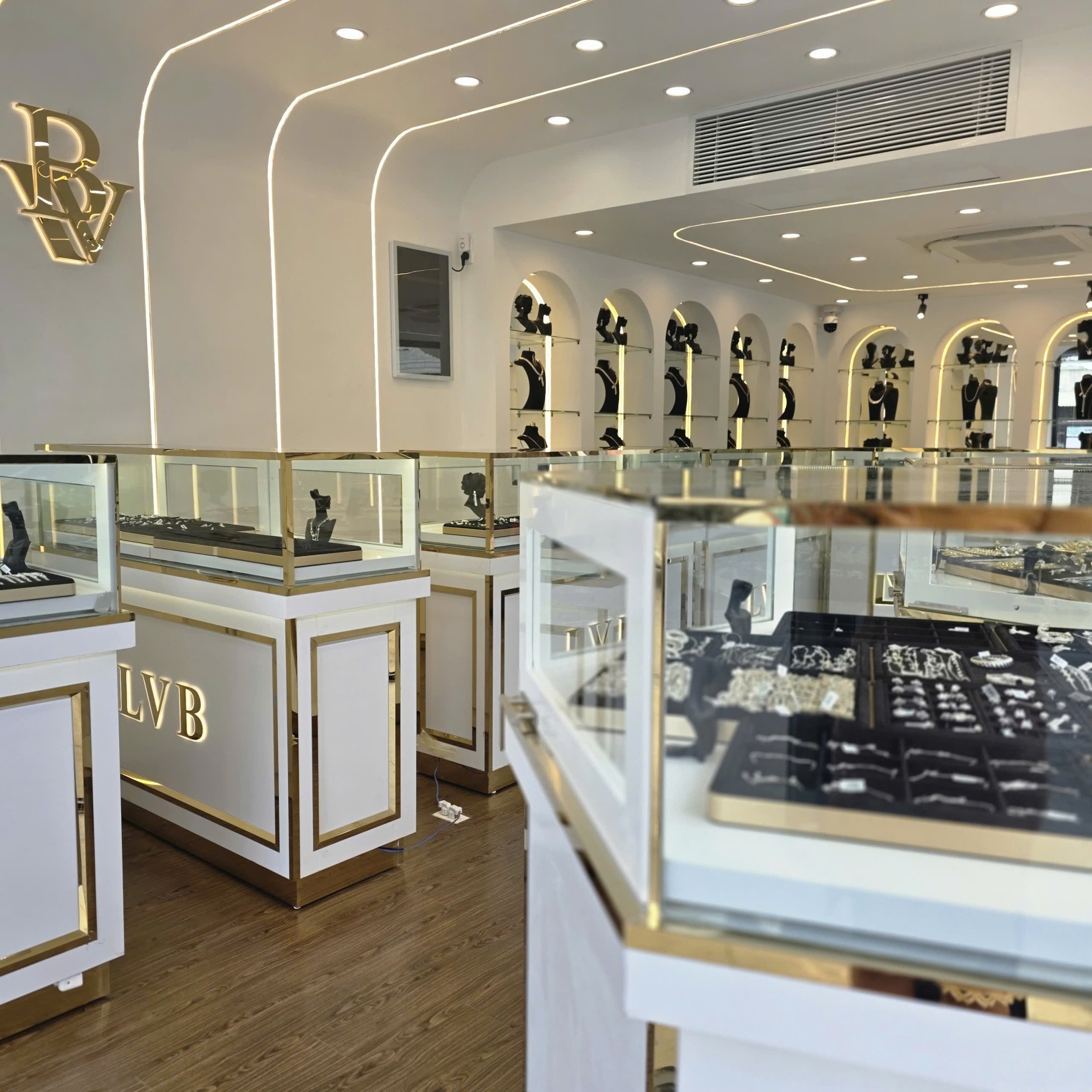 Interior view of a jewelry store with display cases filled with jewelry and necklaces on bust mannequins on wall shelves, bright lighting, and a modern, minimalist design.