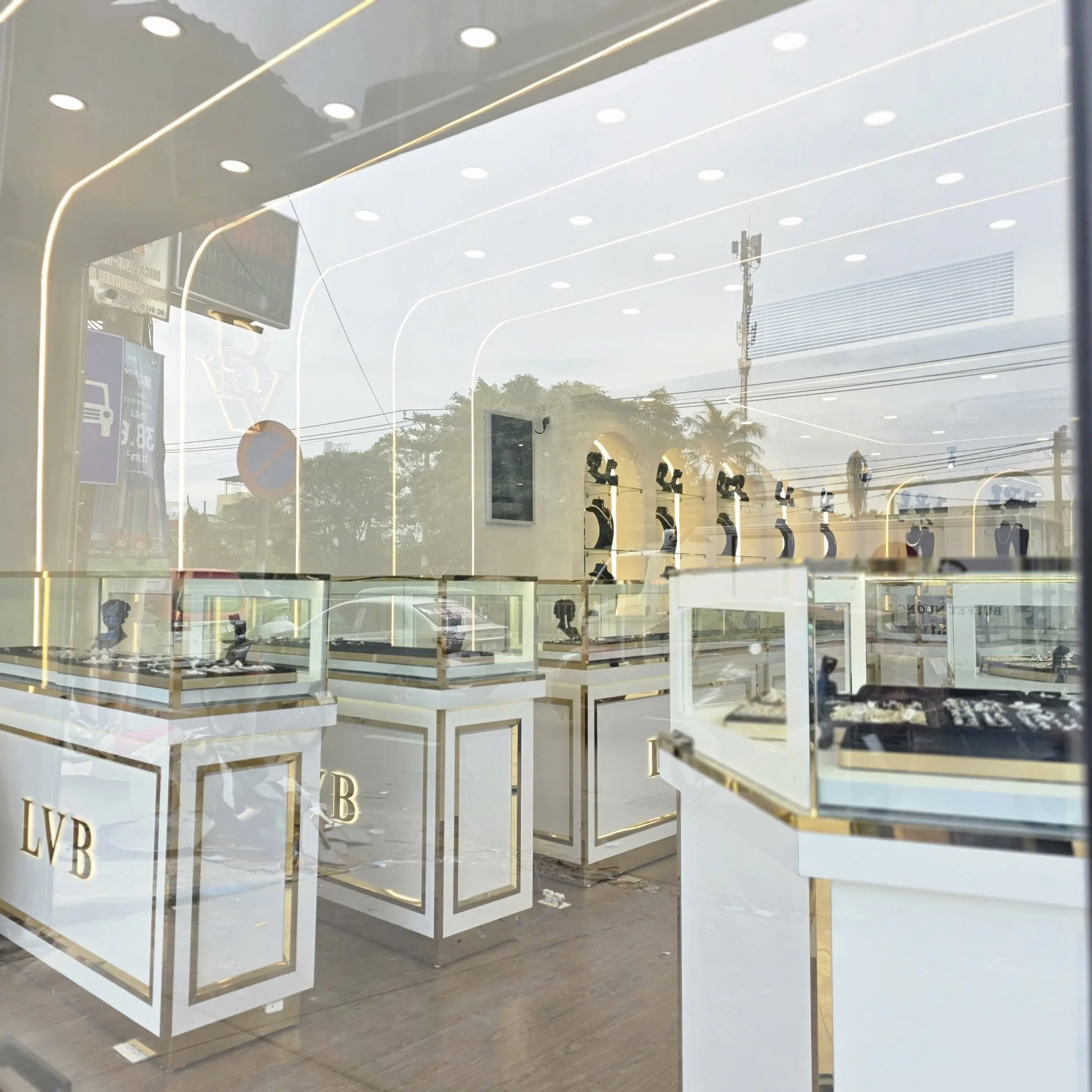 View of jewelry displays inside a store, with glass cases and jewelry on display, seen through a large window with reflections of the outside street and sky.