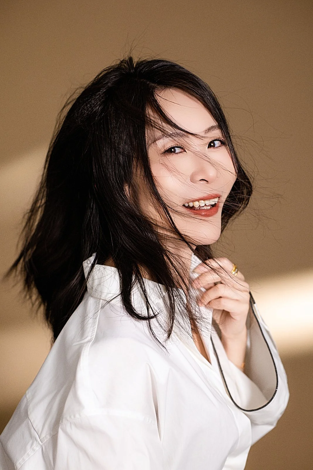A woman with dark hair smiling and looking at the camera, wearing a white shirt against a blurred background.