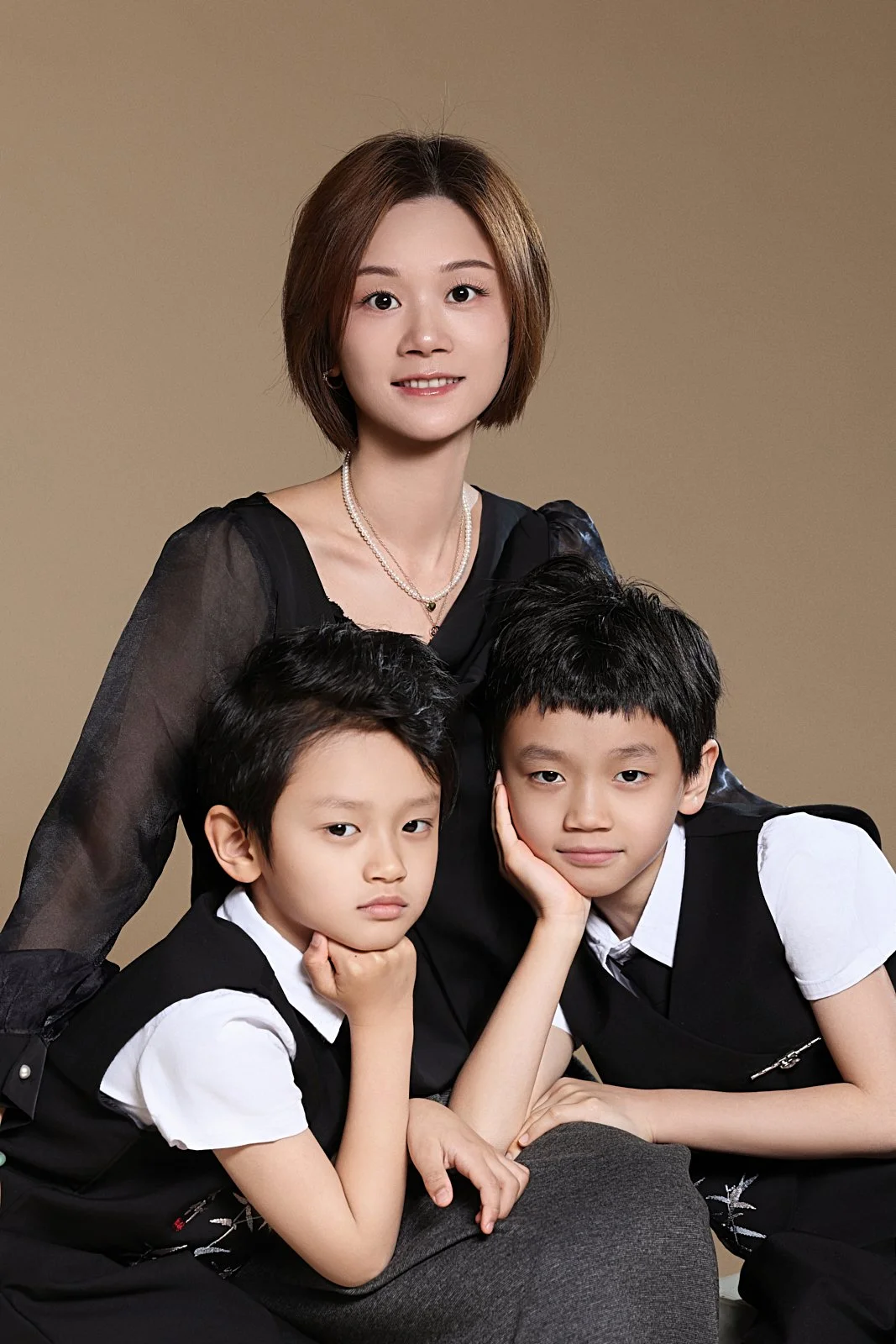 A woman with short brown hair and two young boys, all dressed in black and white, posing together against a plain background.