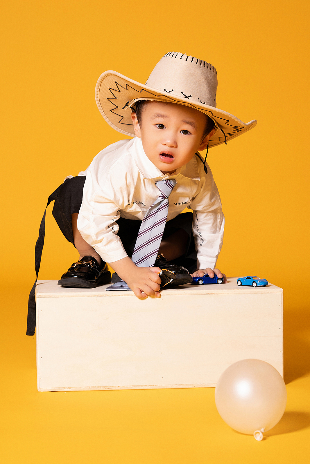 Boy in suspenders leaning against brick wall for stylish children’s photo