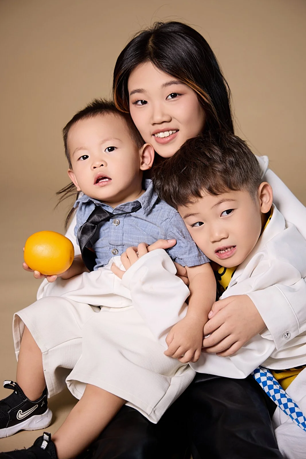 A woman with two young boys, one holding an orange, all posing together against a neutral background.