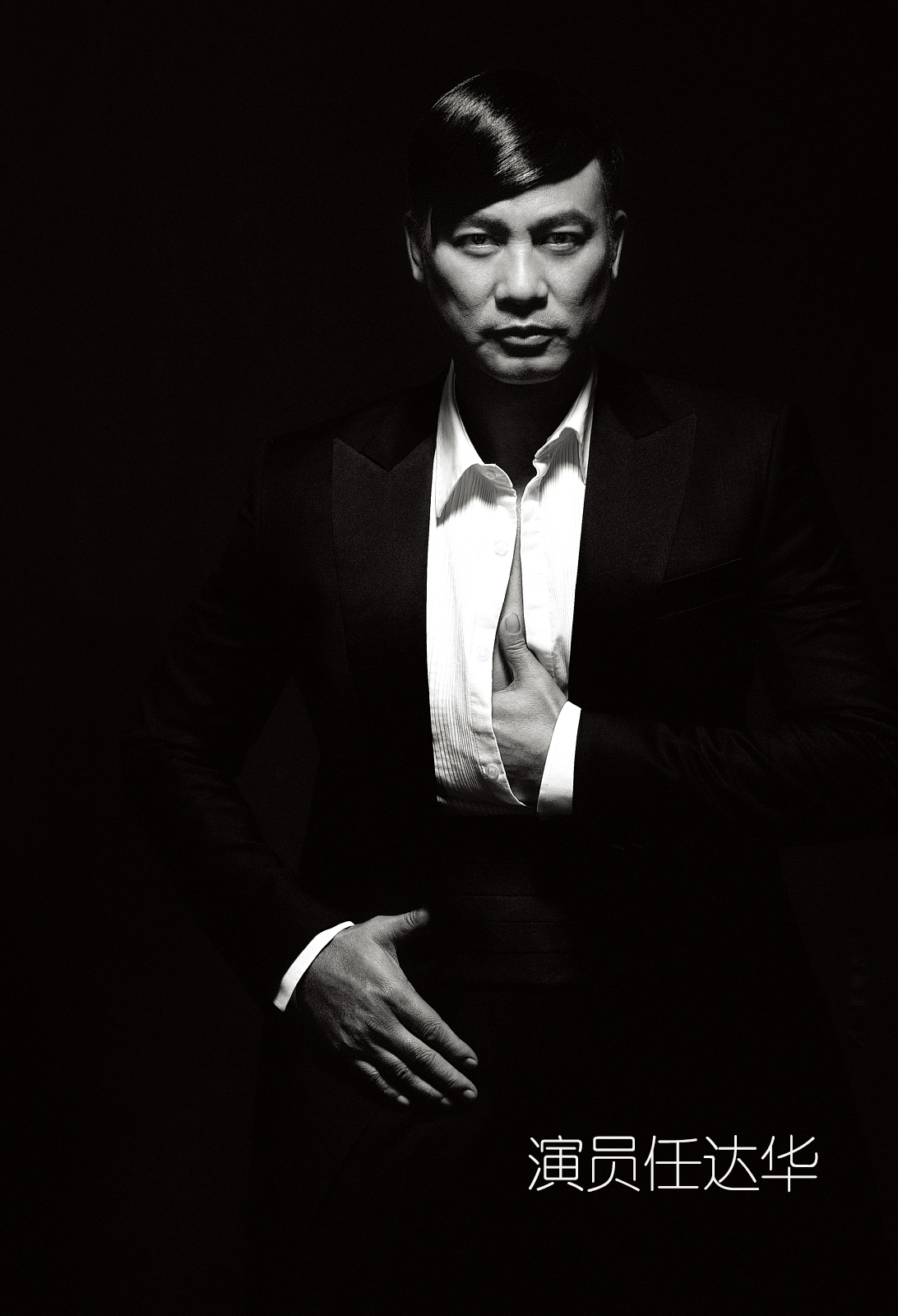 A black and white portrait of a man in a suit, with short hair, posing with one hand on his chest and the other on his waist, against a dark background. There are Chinese characters at the bottom of the image.