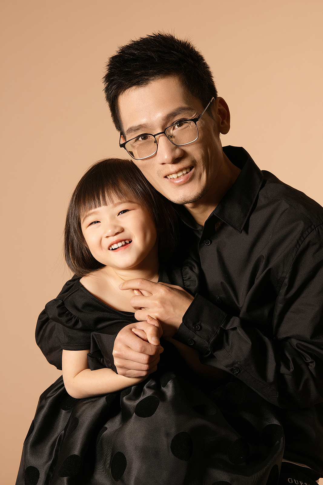 A man and young girl smiling and hugging against a beige background.