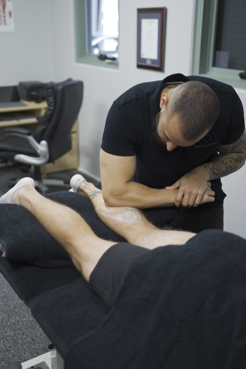 A physical therapist examines a patient's leg while lying on a treatment table in a clinical setting.