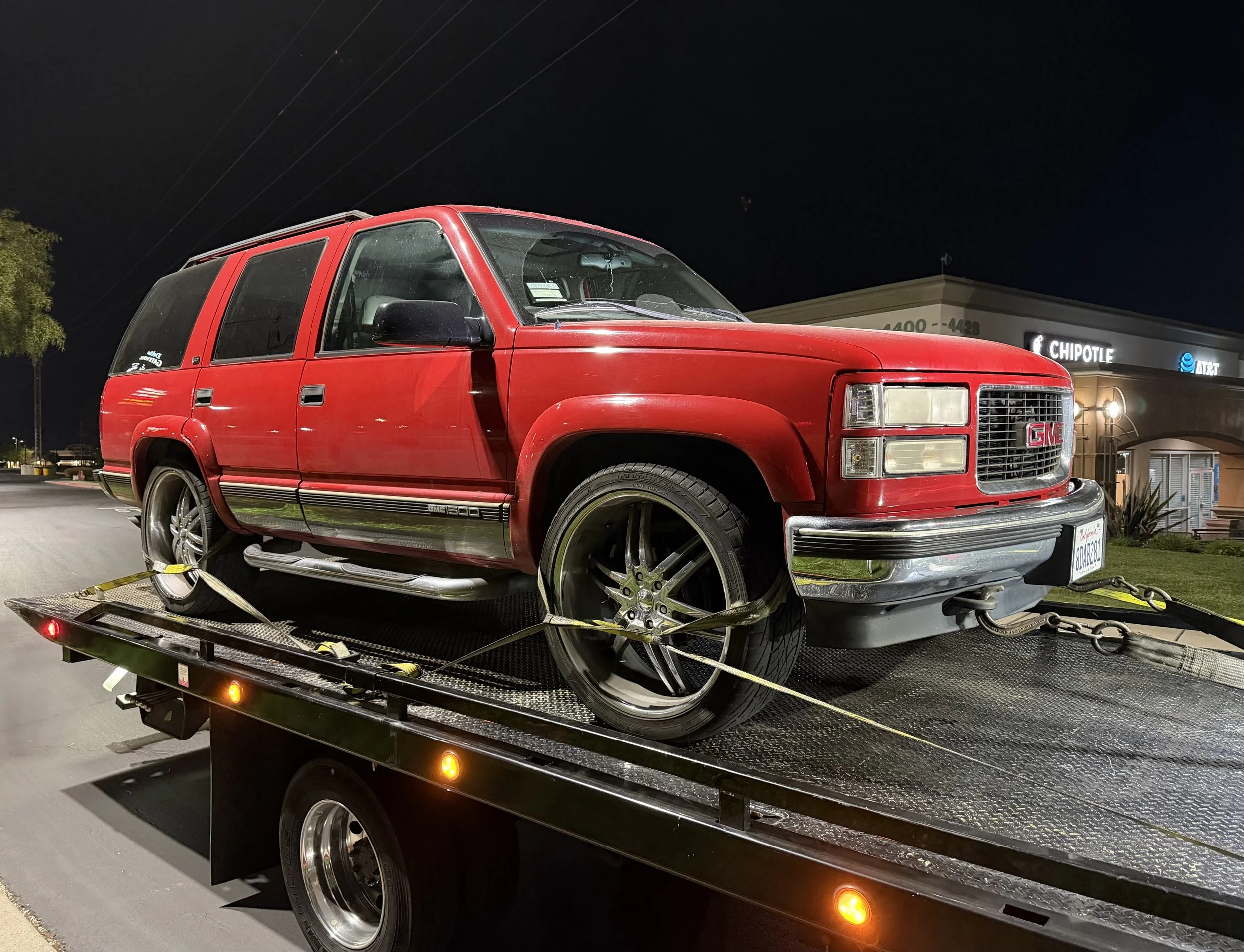 Flatbed towing service in Antioch CA transporting a red GMC Yukon on a 24-7 Rescue Towing flatbed tow truck at night.