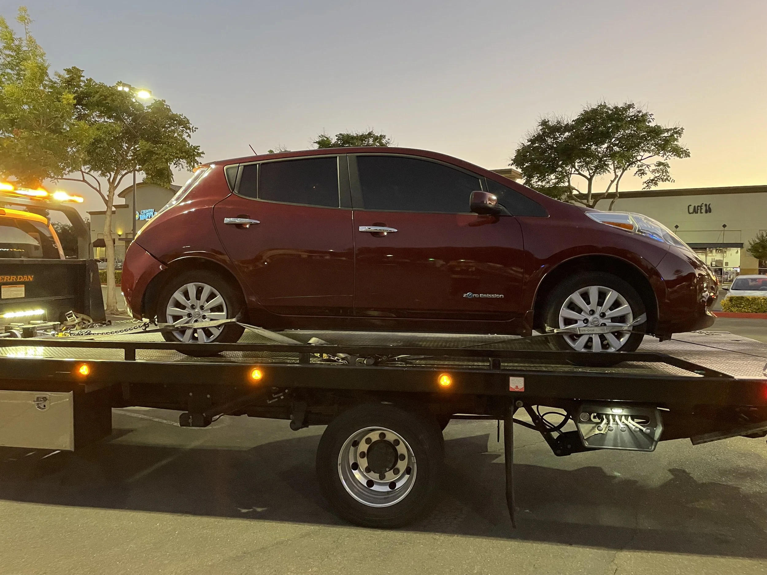 Tow truck near me service in Antioch California transporting a Nissan Leaf electric vehicle on a flatbed tow truck during evening roadside assistance.
