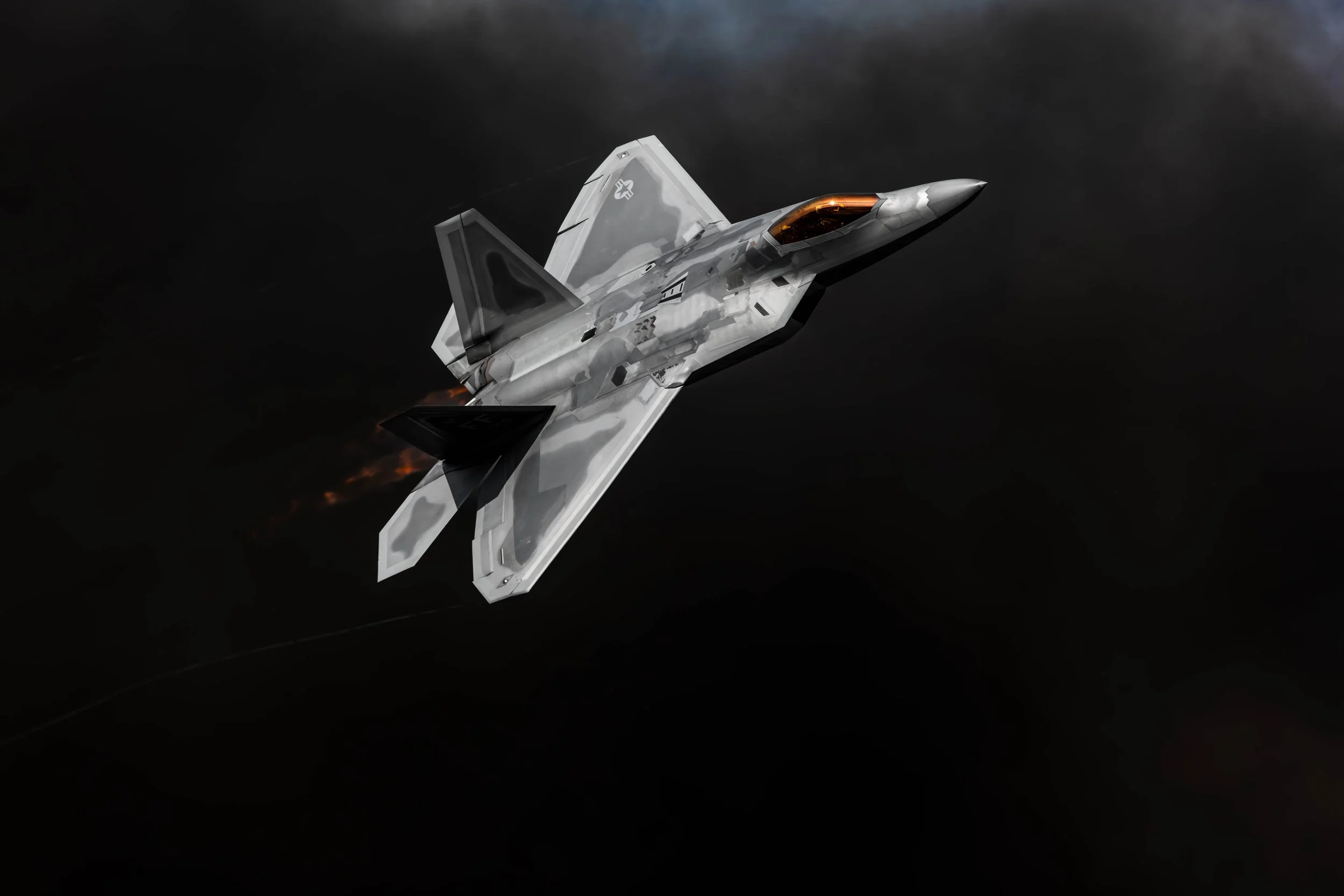 A military fighter jet flying at high speed through dark sky, with flames visible at the jet's engines.