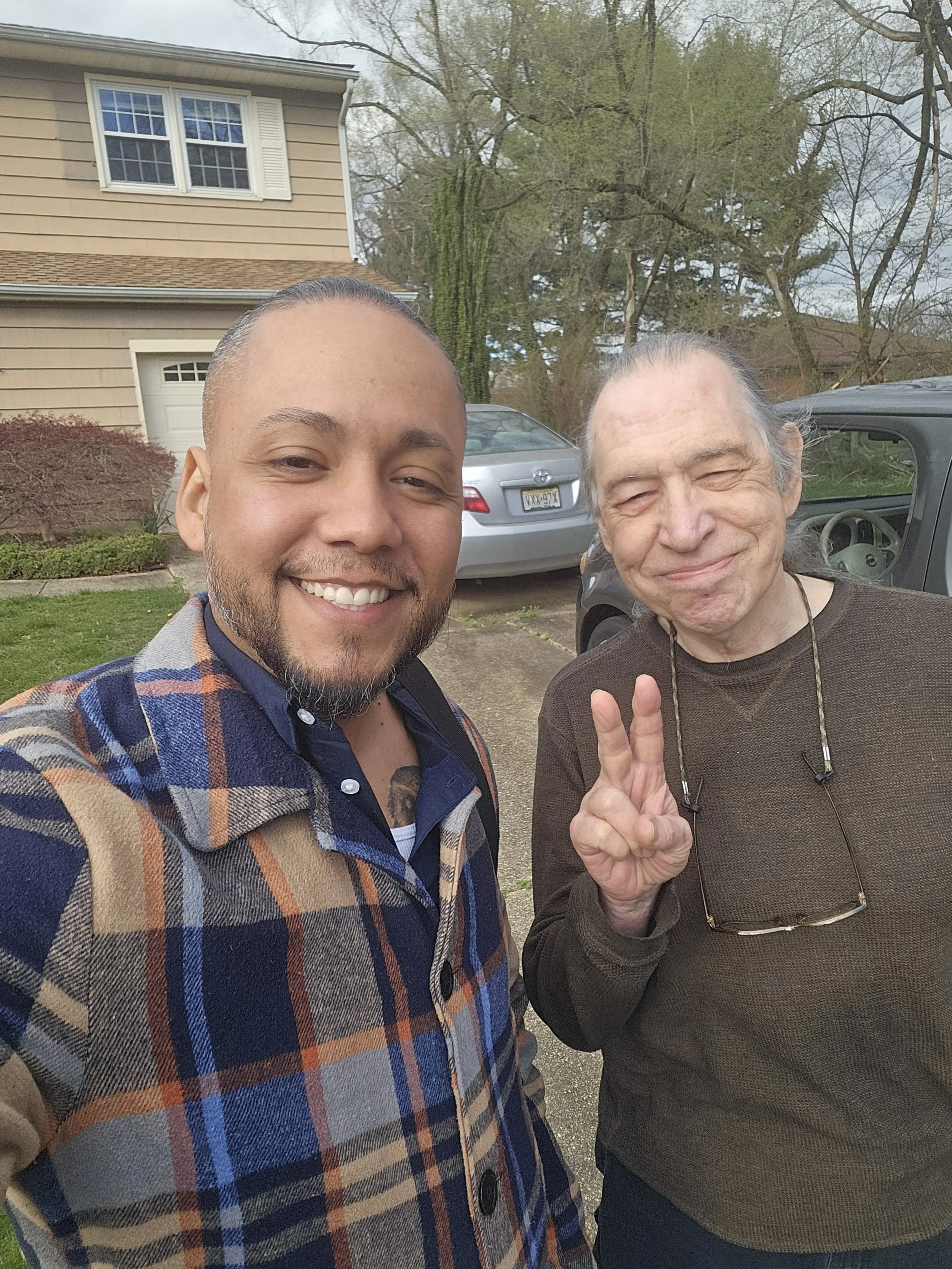 Solar consultant smiles with a satisfied New Jersey homeowner flashing a peace sign after a successful solar consultation, with a suburban home and driveway in the background.
