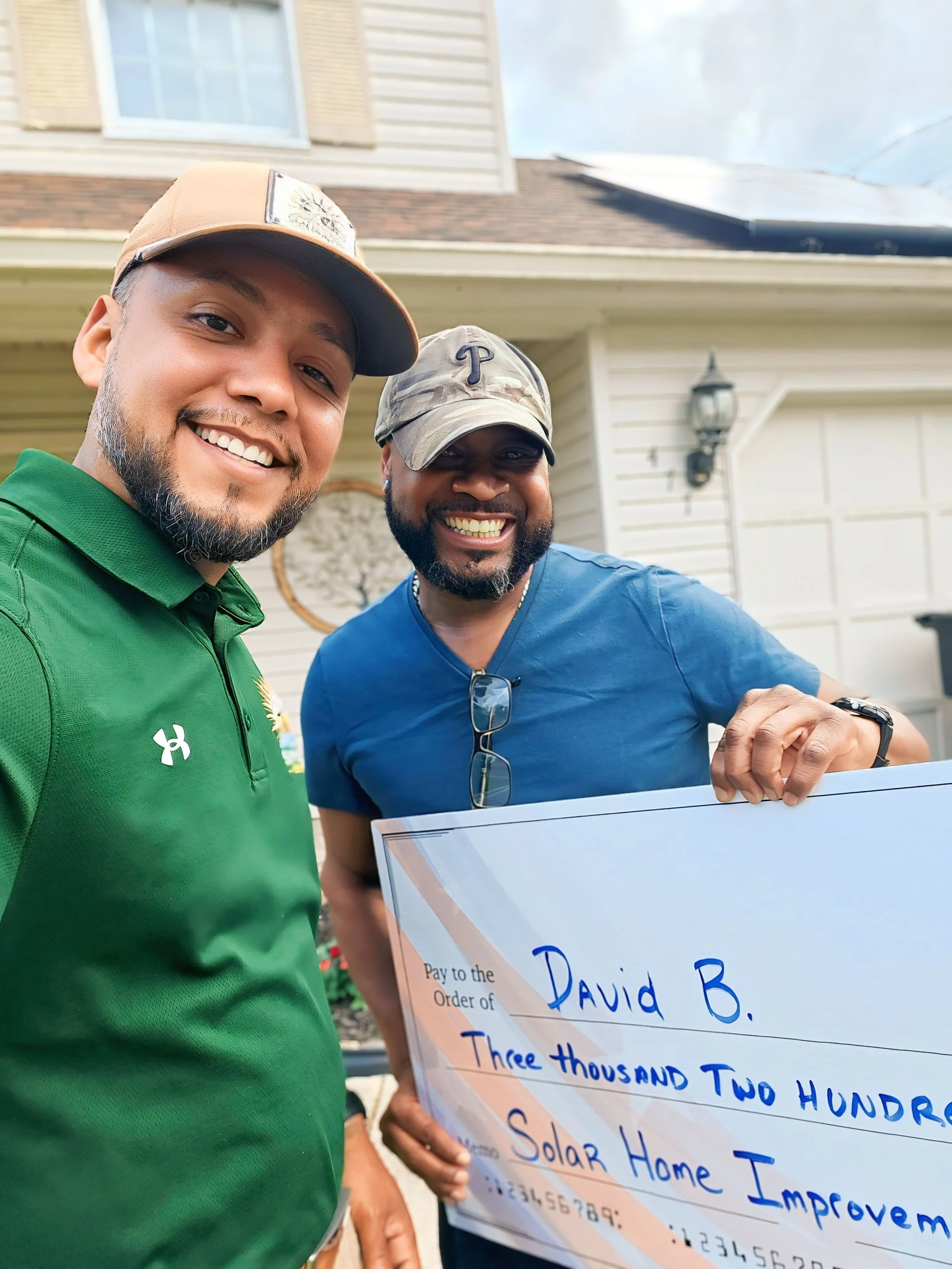 Jose the Sun Hunter stands with happy homeowner David B., holding a large check for $3,200 toward solar home improvements. Rooftop solar panels visible in the background, highlighting real savings and financial incentives.
