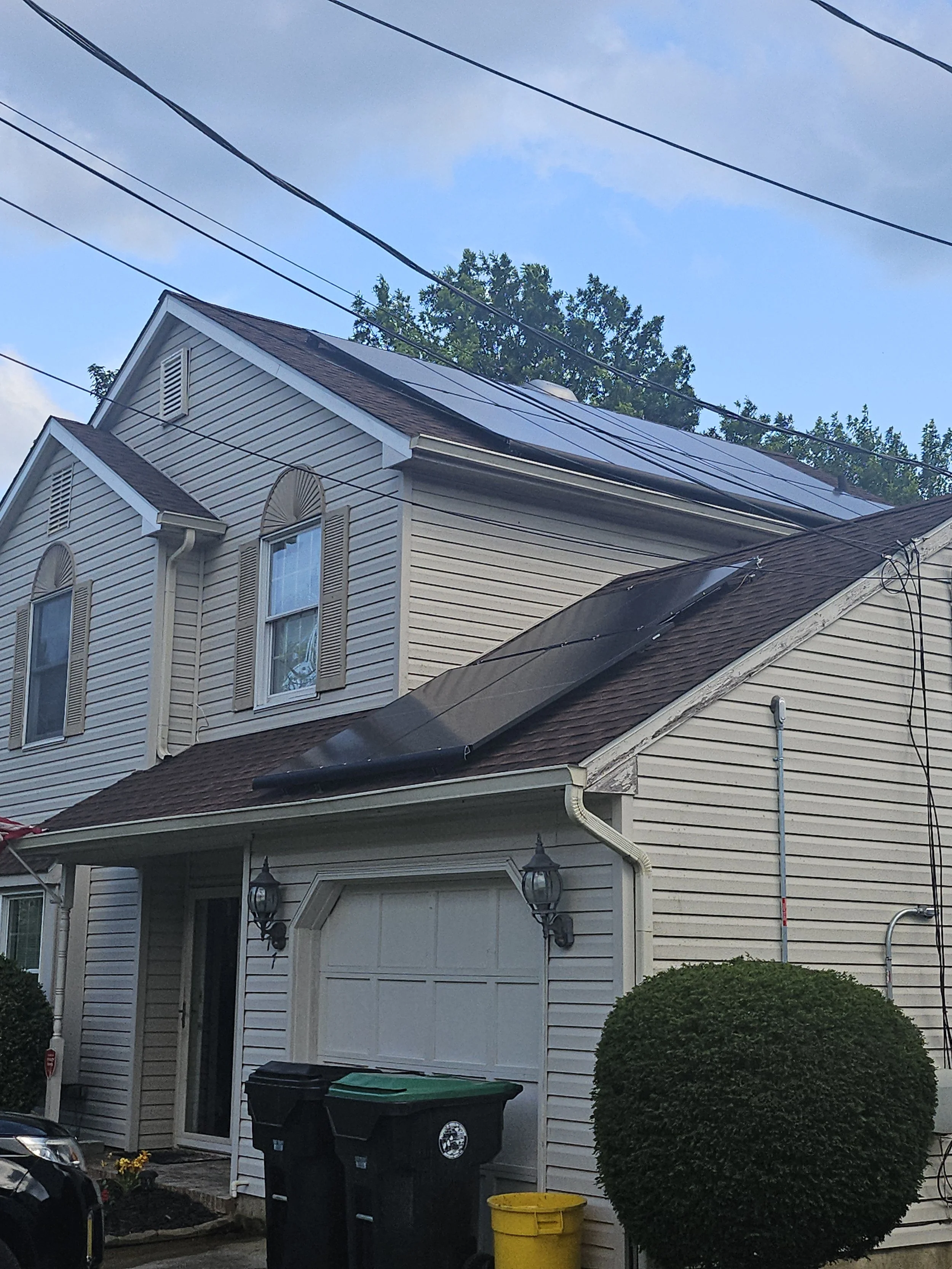 Suburban two-story home with rooftop solar panels installed on multiple roof sections, showcasing a clean energy upgrade in a residential neighborhood under partly cloudy skies.