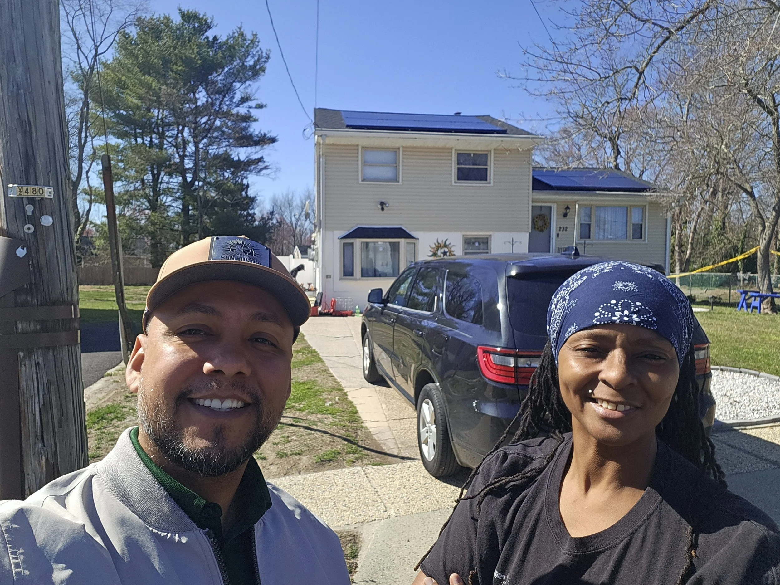 Happy solar consultant and homeowner standing in front of a residential home with newly installed rooftop solar panels, celebrating a successful solar panel installation on a sunny day.