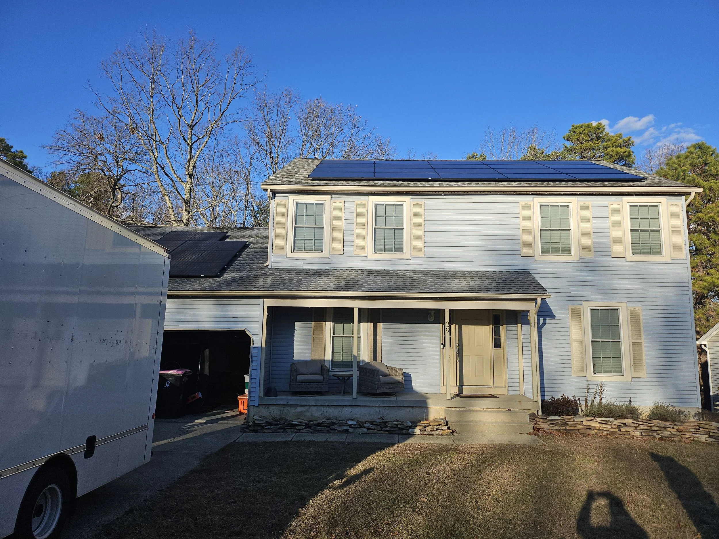 Two-story suburban home in New Jersey equipped with rooftop solar panels on both garage and main roof, showcasing a complete residential solar installation on a sunny winter day